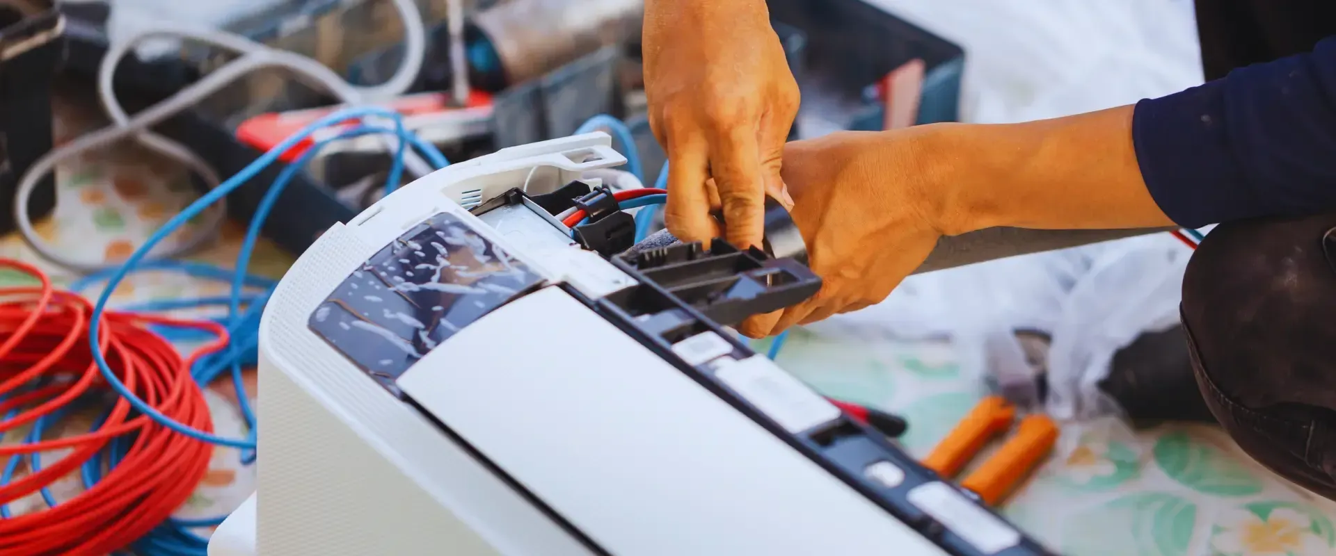 A man is fixing an air conditioner with a pair of pliers.