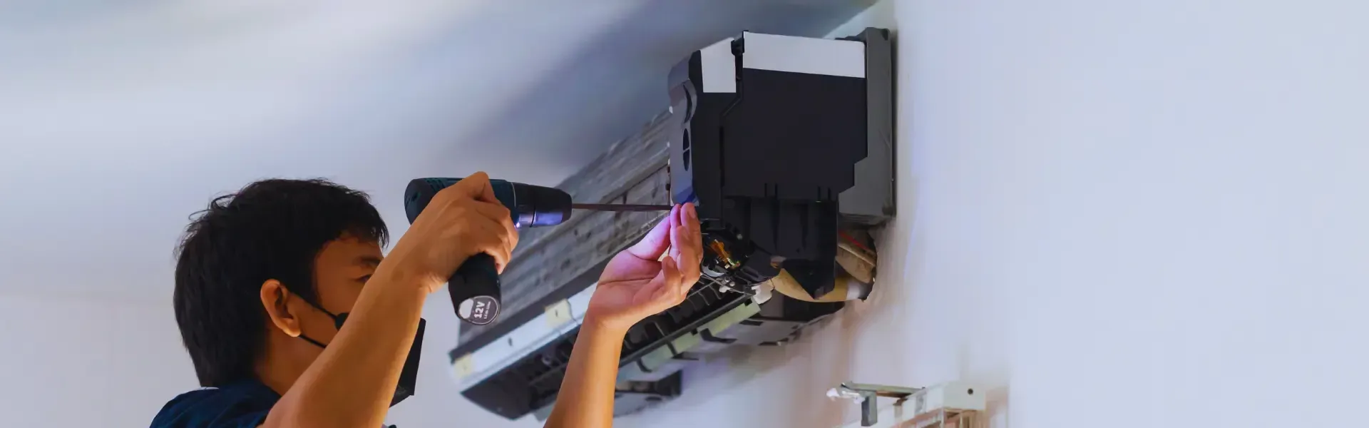 A man is fixing an air conditioner with a screwdriver.