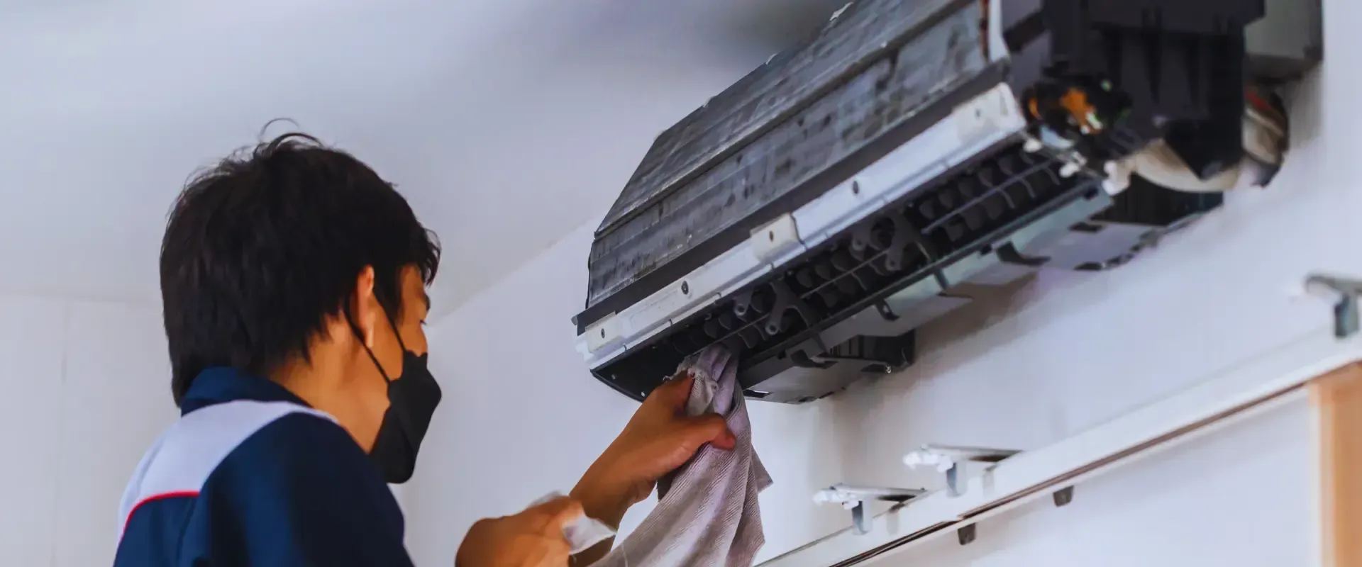 A man wearing a mask is cleaning an air conditioner.