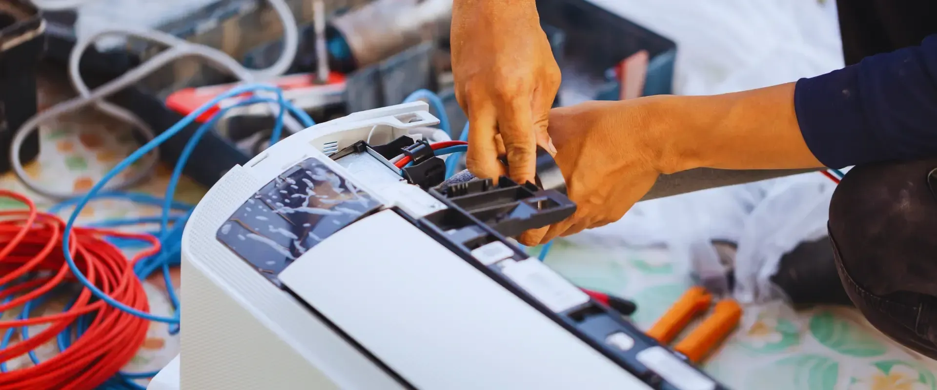 A man is fixing an air conditioner with a pair of pliers.