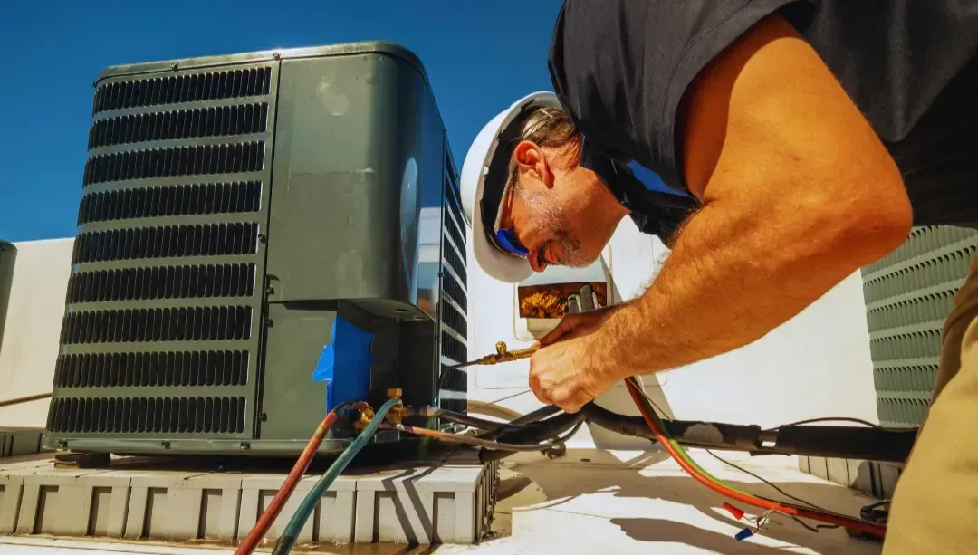 A man is working on an air conditioner on the roof of a building.