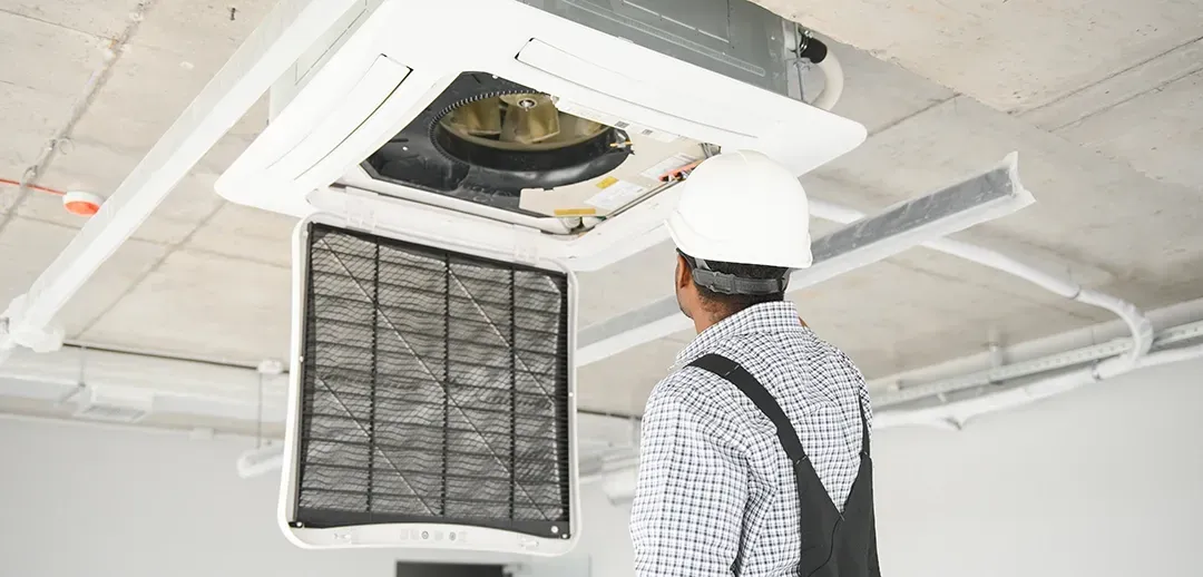 A man in a hard hat is working on an air conditioner.