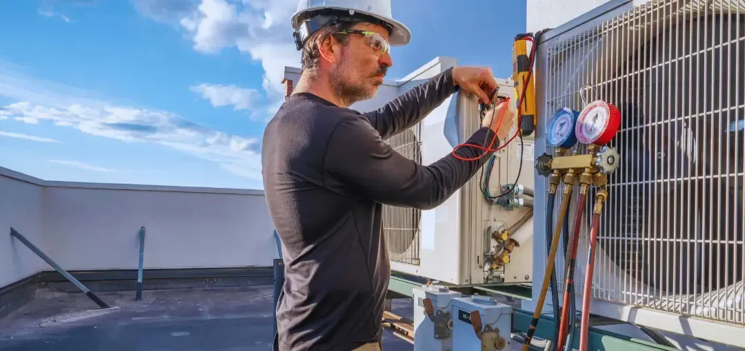 A man is working on an air conditioner on top of a building.