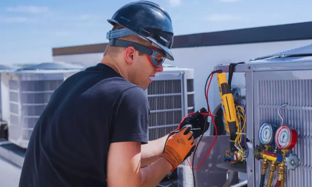 A man wearing a hard hat and goggles is working on an air conditioner.