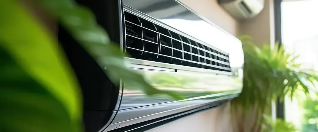 A close up of an air conditioner hanging on a wall next to a plant.