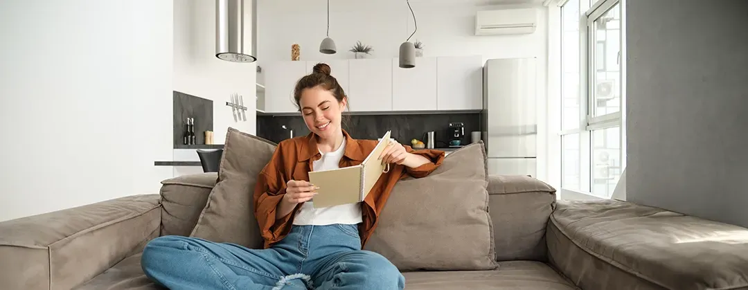 A woman is sitting on a couch reading a book.