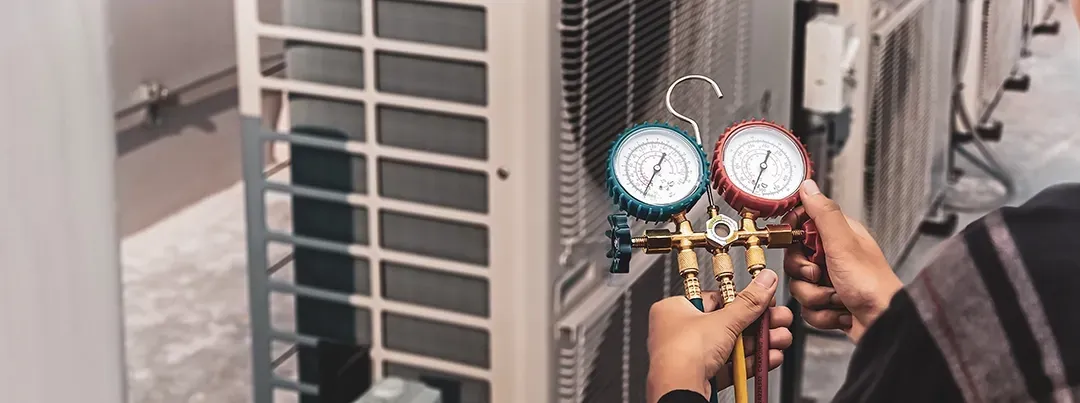 A man is holding two gauges in front of an air conditioner.