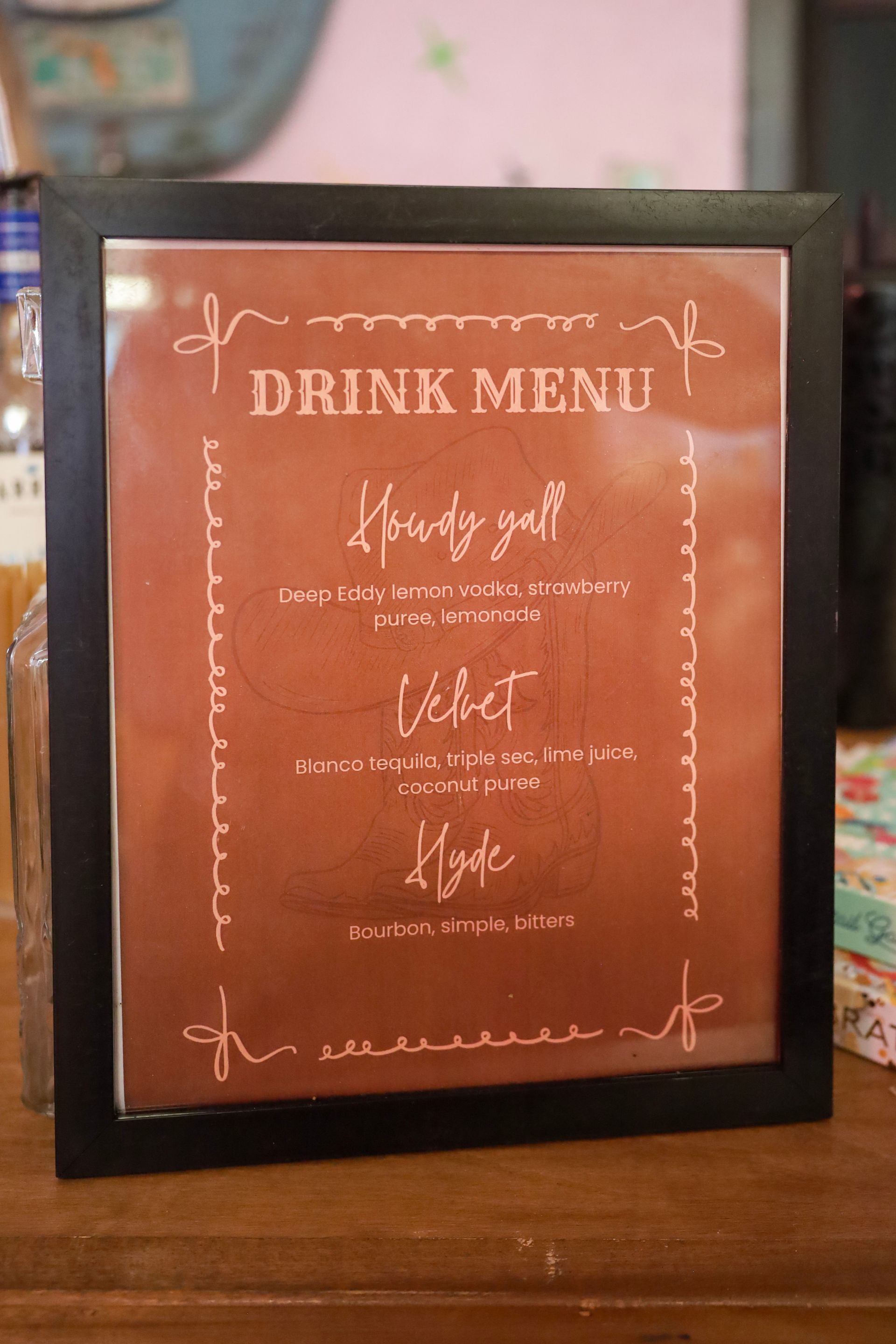 Framed orange drink menu sign on a wooden table, listing latte, coffee, and tea options