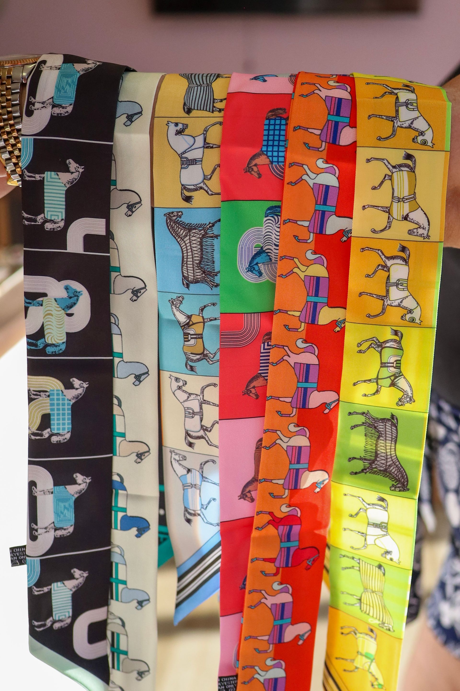 Colorful dog-print scarves or fabric strips hanging vertically in black, teal, beige, red, orange, and yellow.