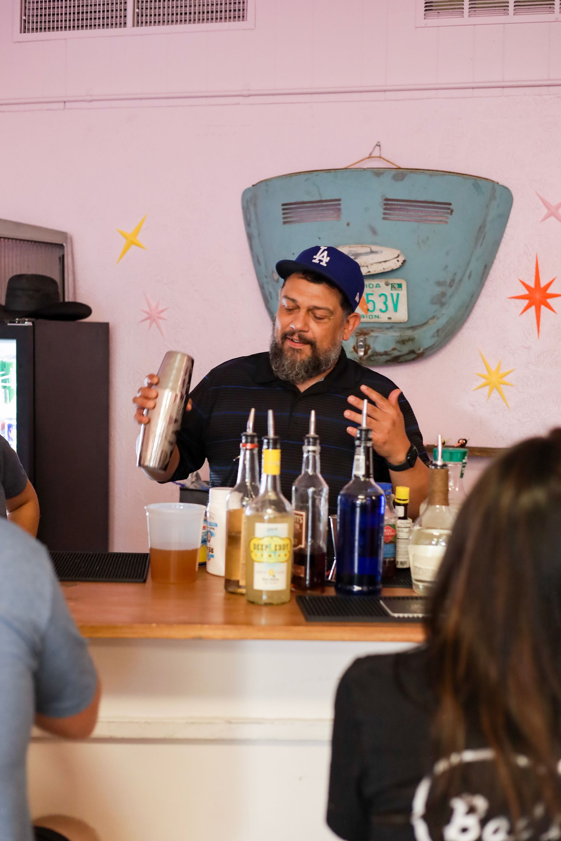 Bartender shaking a drink behind a bar with bottles lined up on the counter.