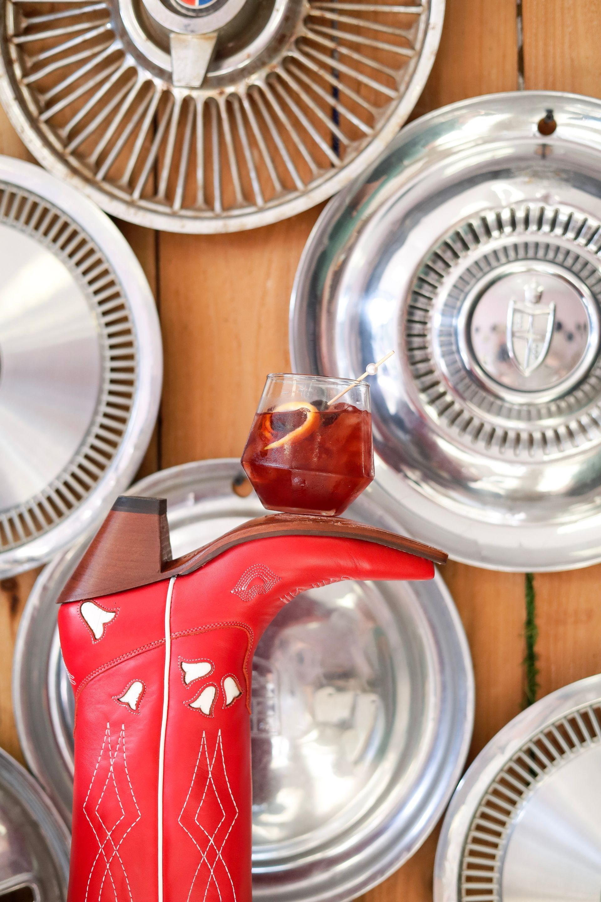 Red kettle on a wooden table with shiny silver trays hanging on the wall and a glass candle holder on top