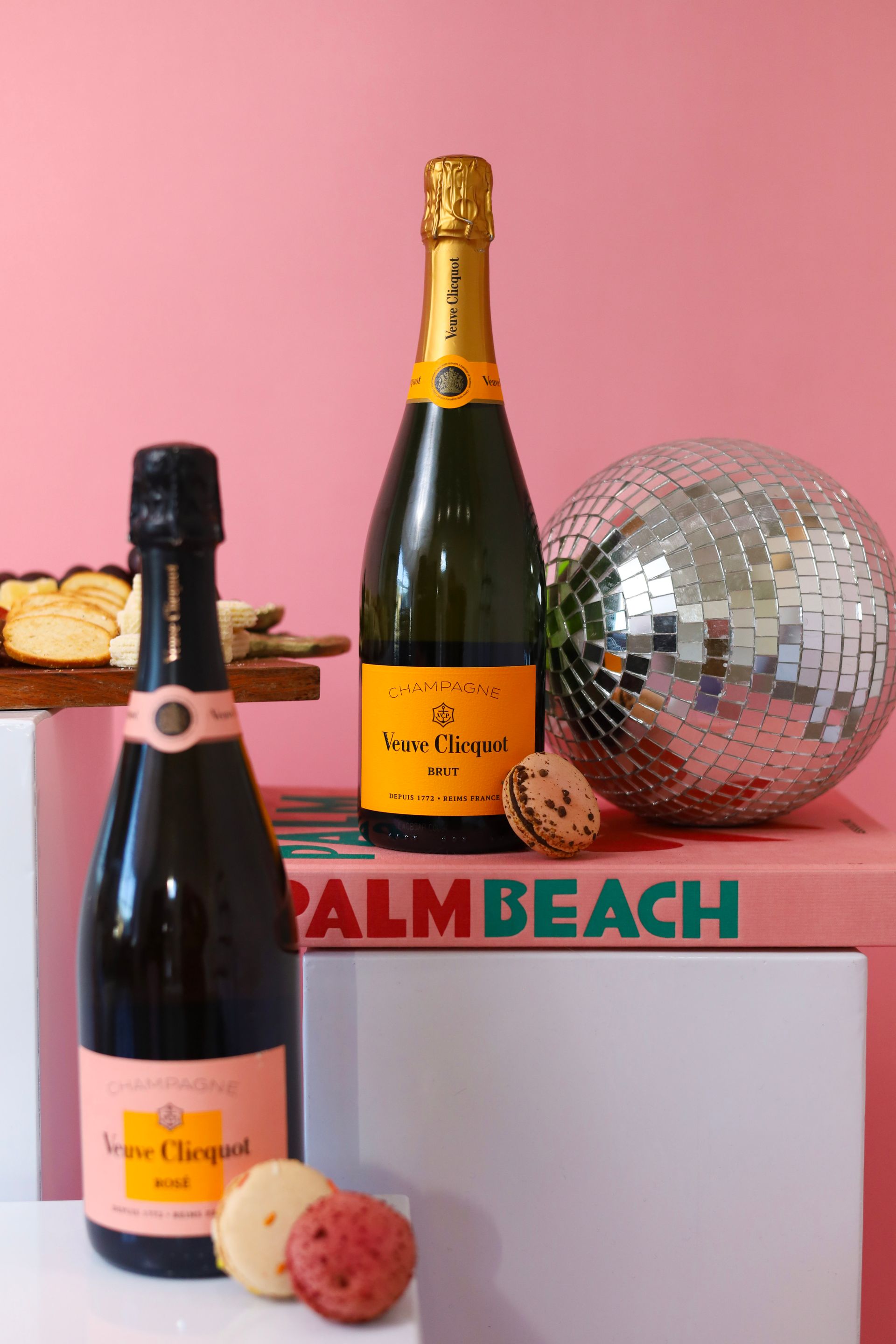 Two champagne bottles, a disco ball, and cookies on a pink shelf labeled “PALM BEACH”