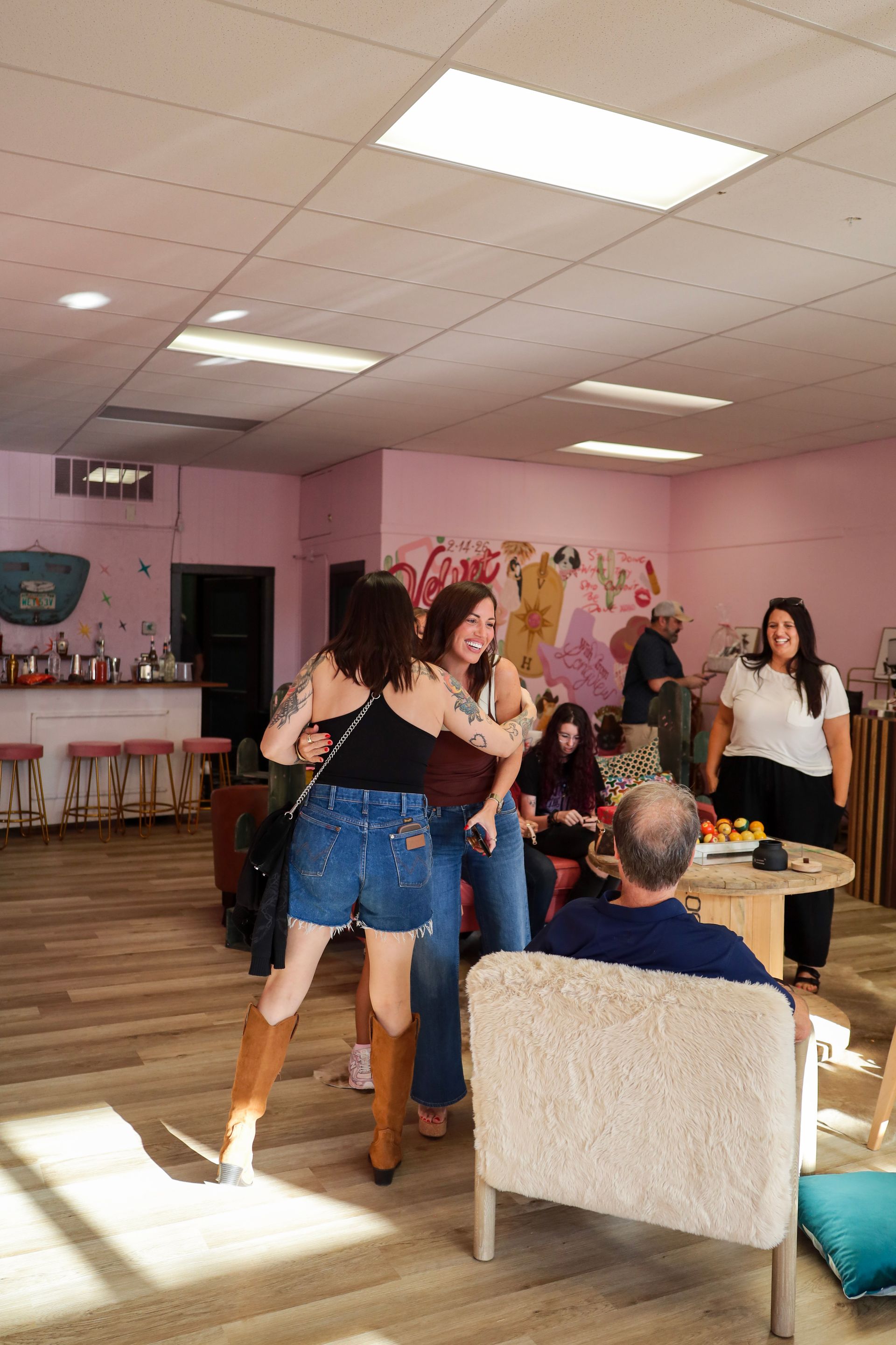 People dancing in a pink party room while seated guests watch from sofas and chairs.