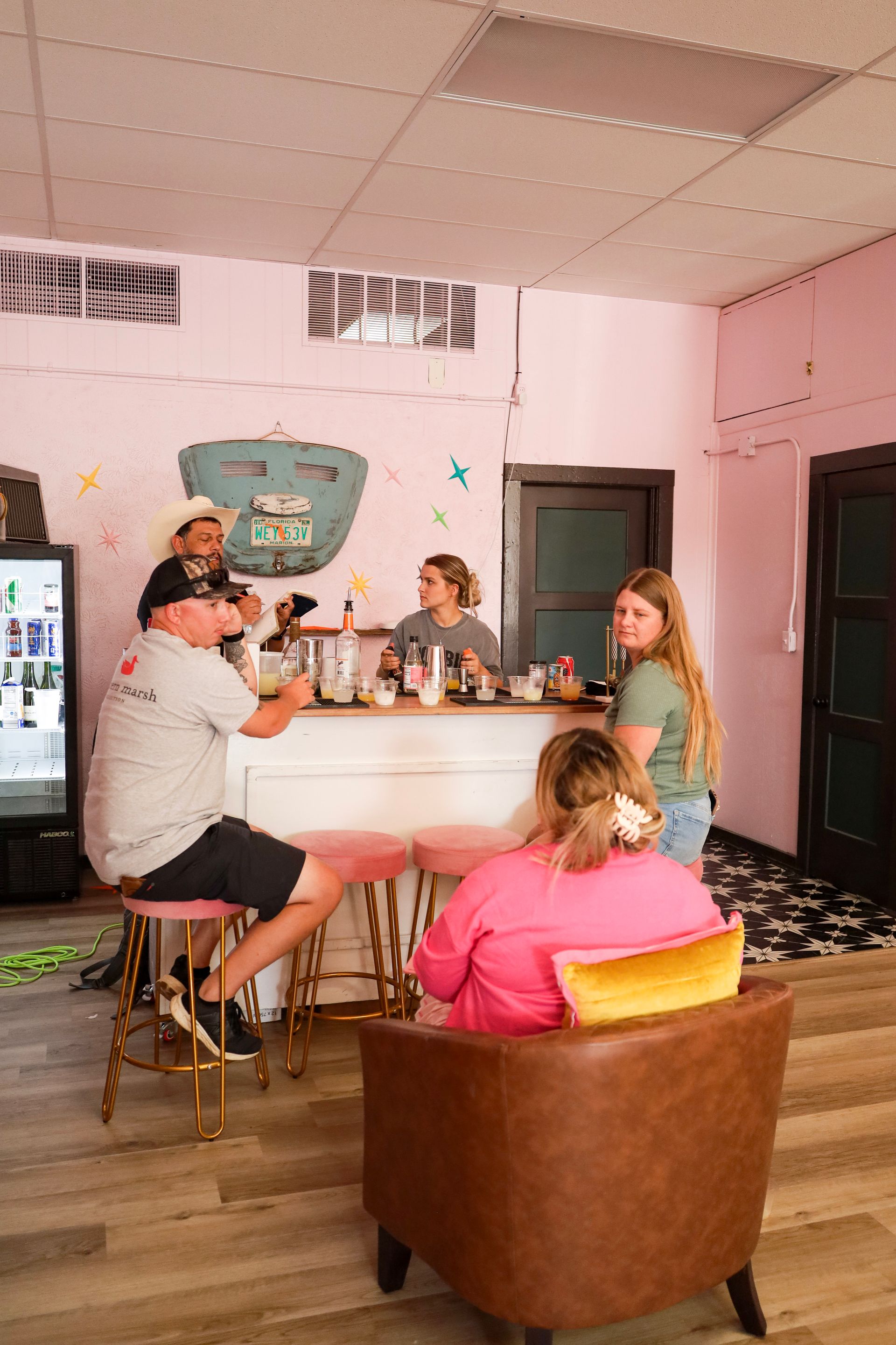 People gathered around a bar in a pink-walled room, chatting and drinking.