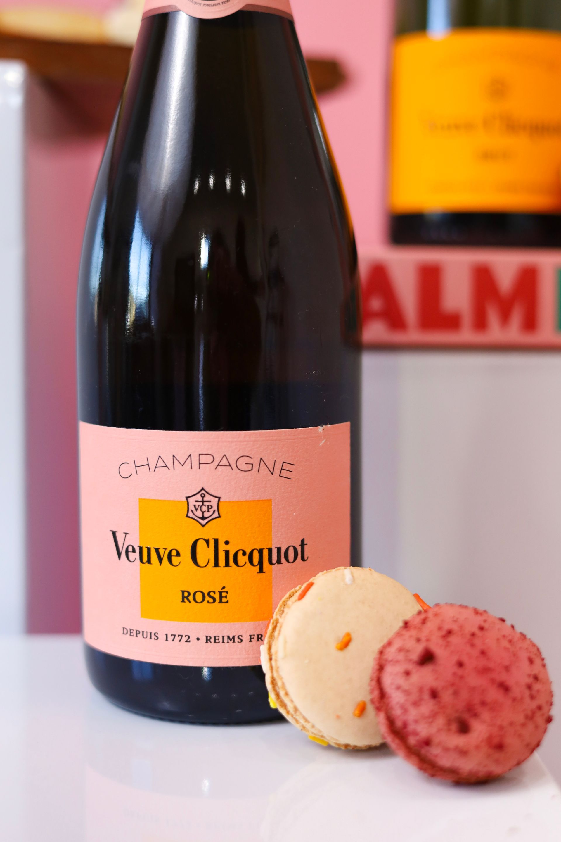 Veuve Clicquot Rosé champagne bottle beside two macarons on a pink surface