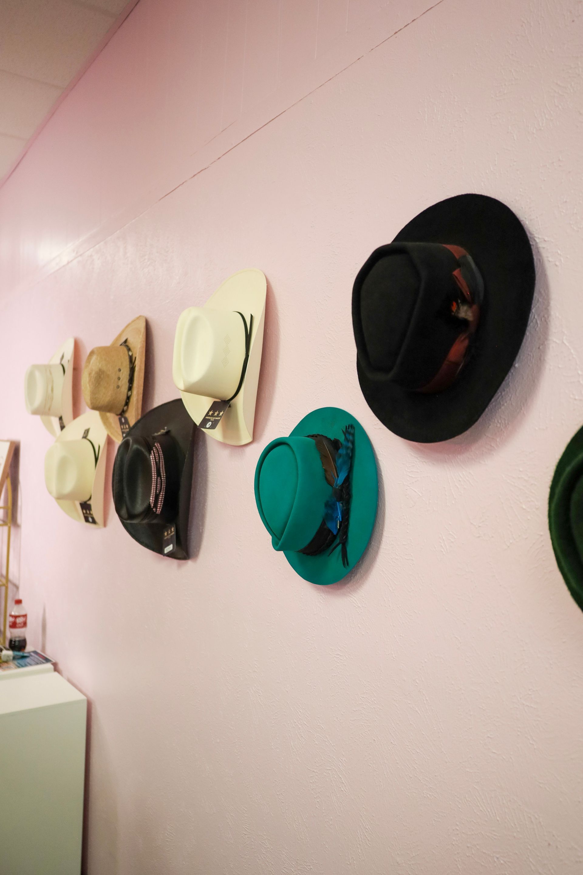 Row of colorful hats hanging on a pink wall in a hallway