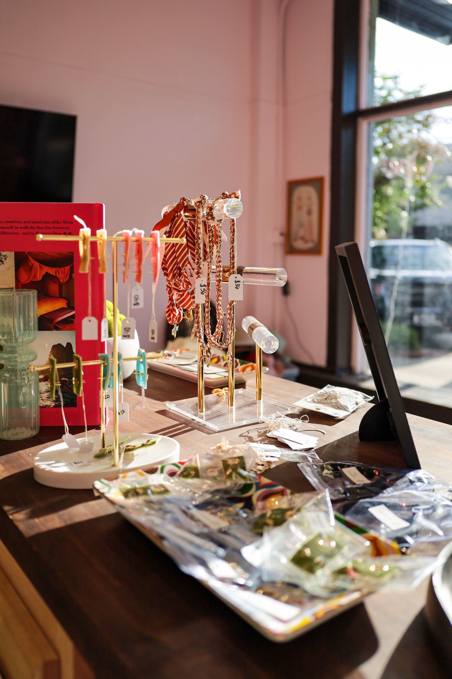 Jewelry display on a table in a bright shop window, with necklaces, rings, and trays of accessories.