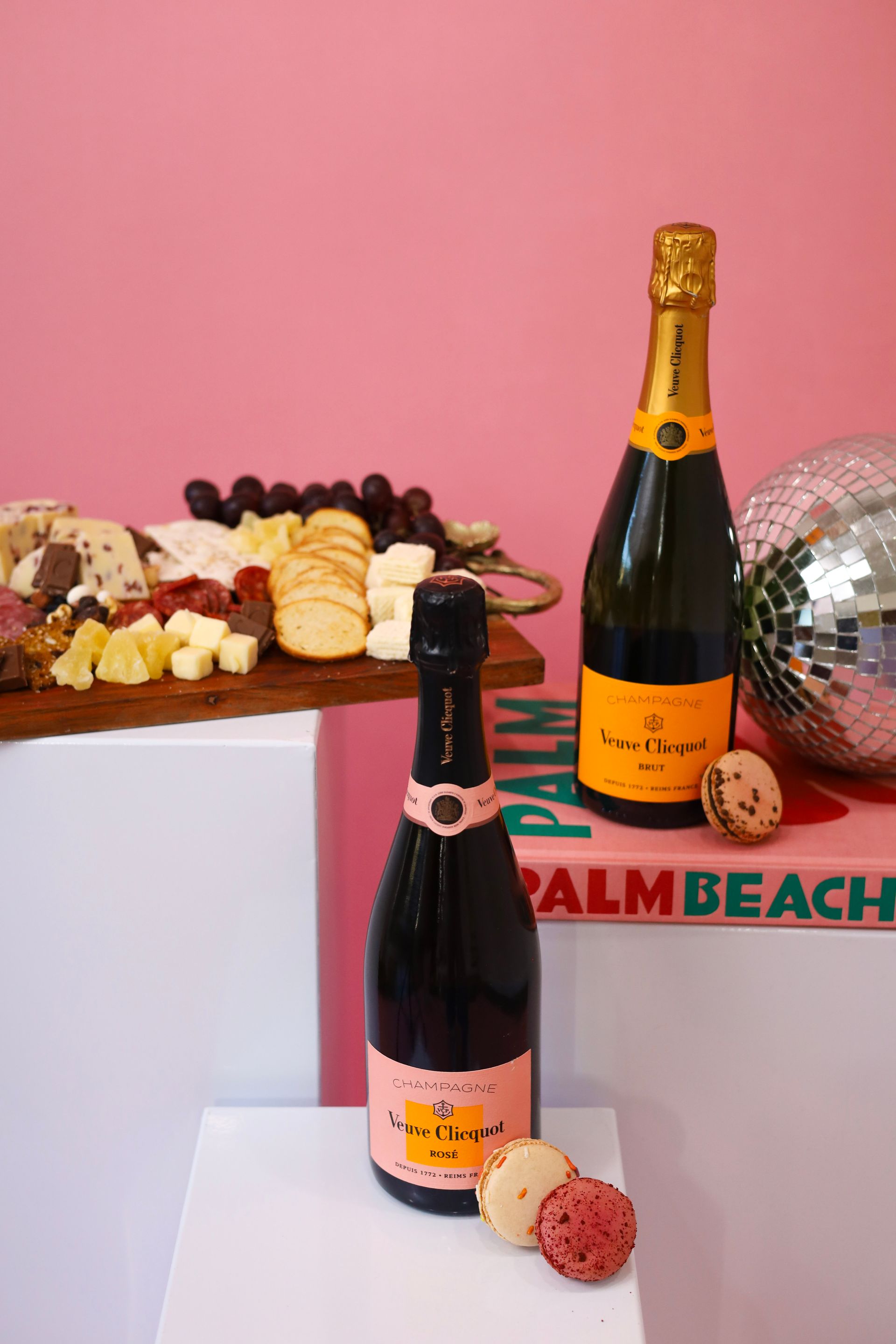 Two bottles of sparkling wine on a pink backdrop with chocolates and a disco ball
