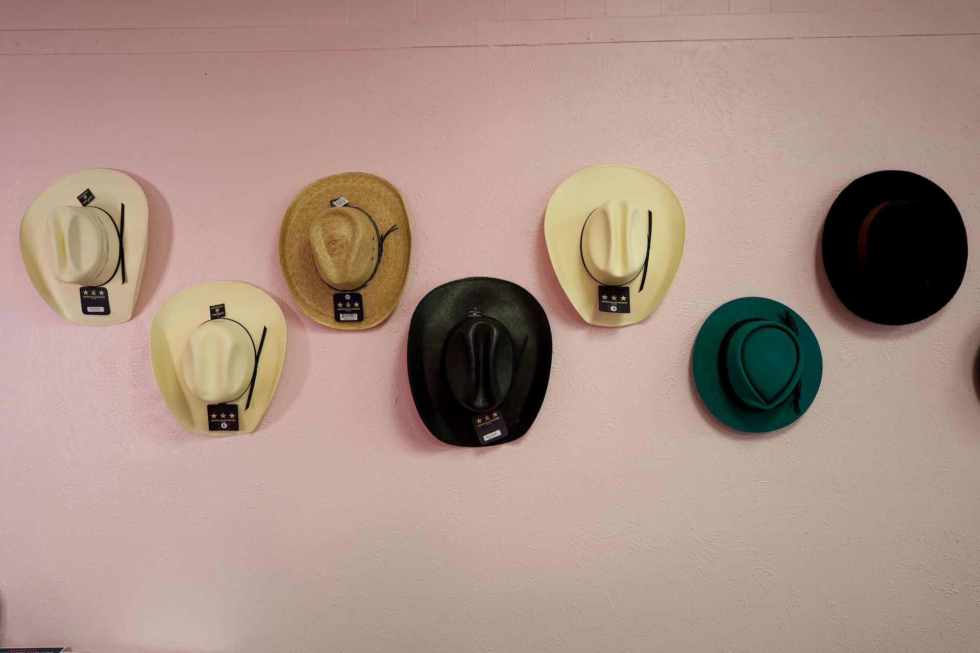 Six hats hanging on a pink wall, arranged in two rows.