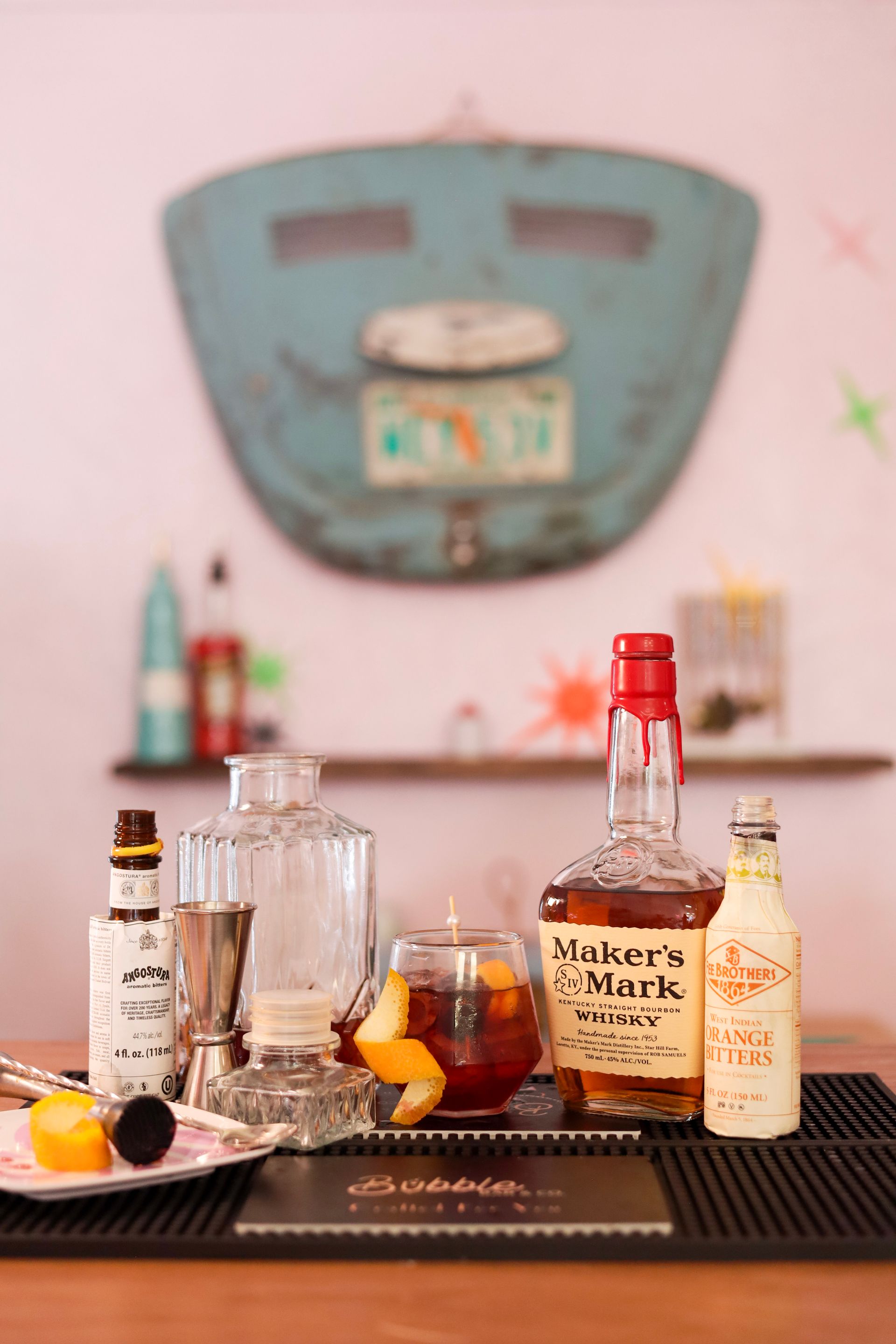 Bar cart with liquor bottles, glasses, citrus, and a teal vintage suitcase in the background