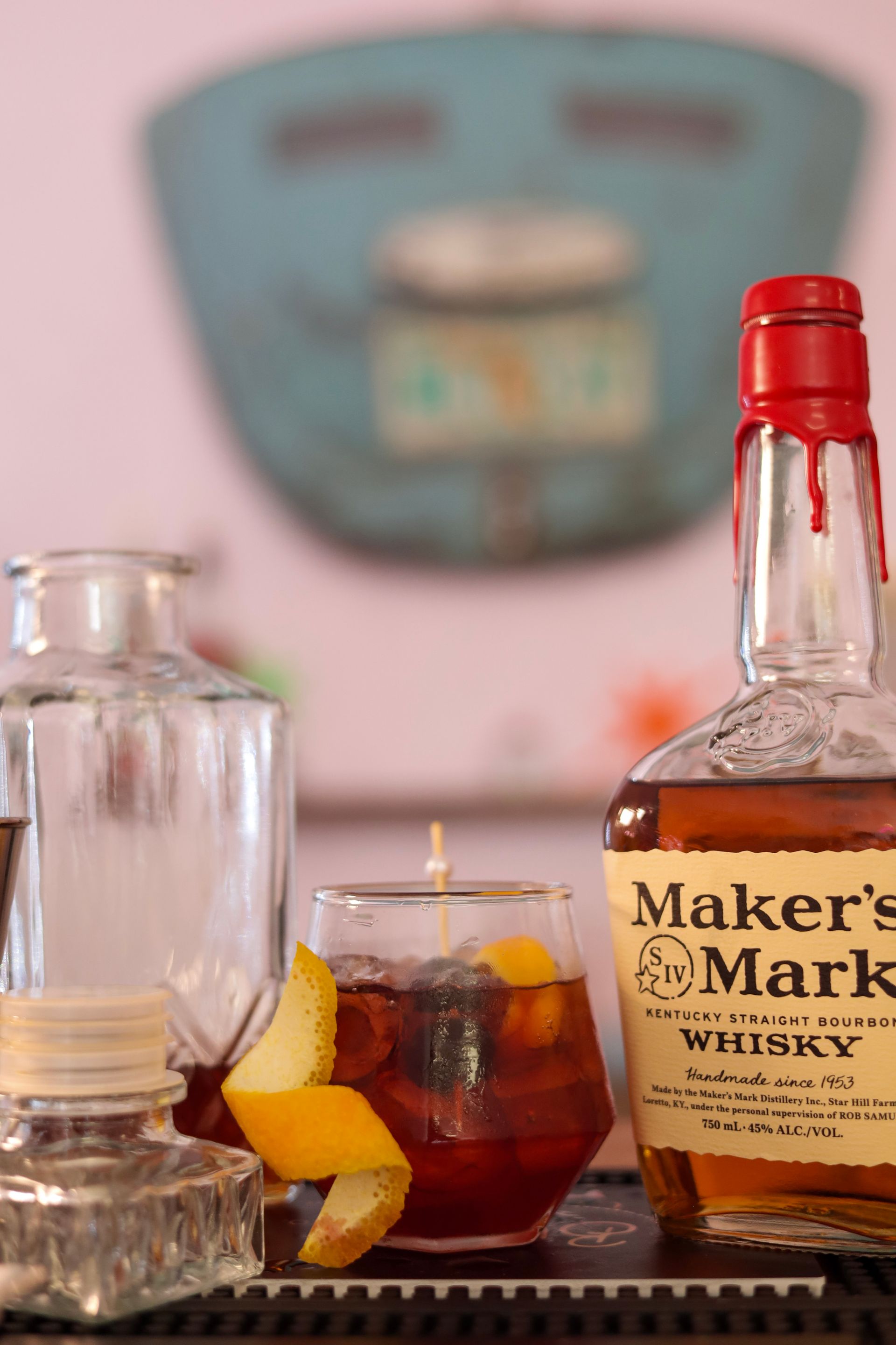 Whiskey bottle and cocktail with orange peel on a table beside a glass decanter