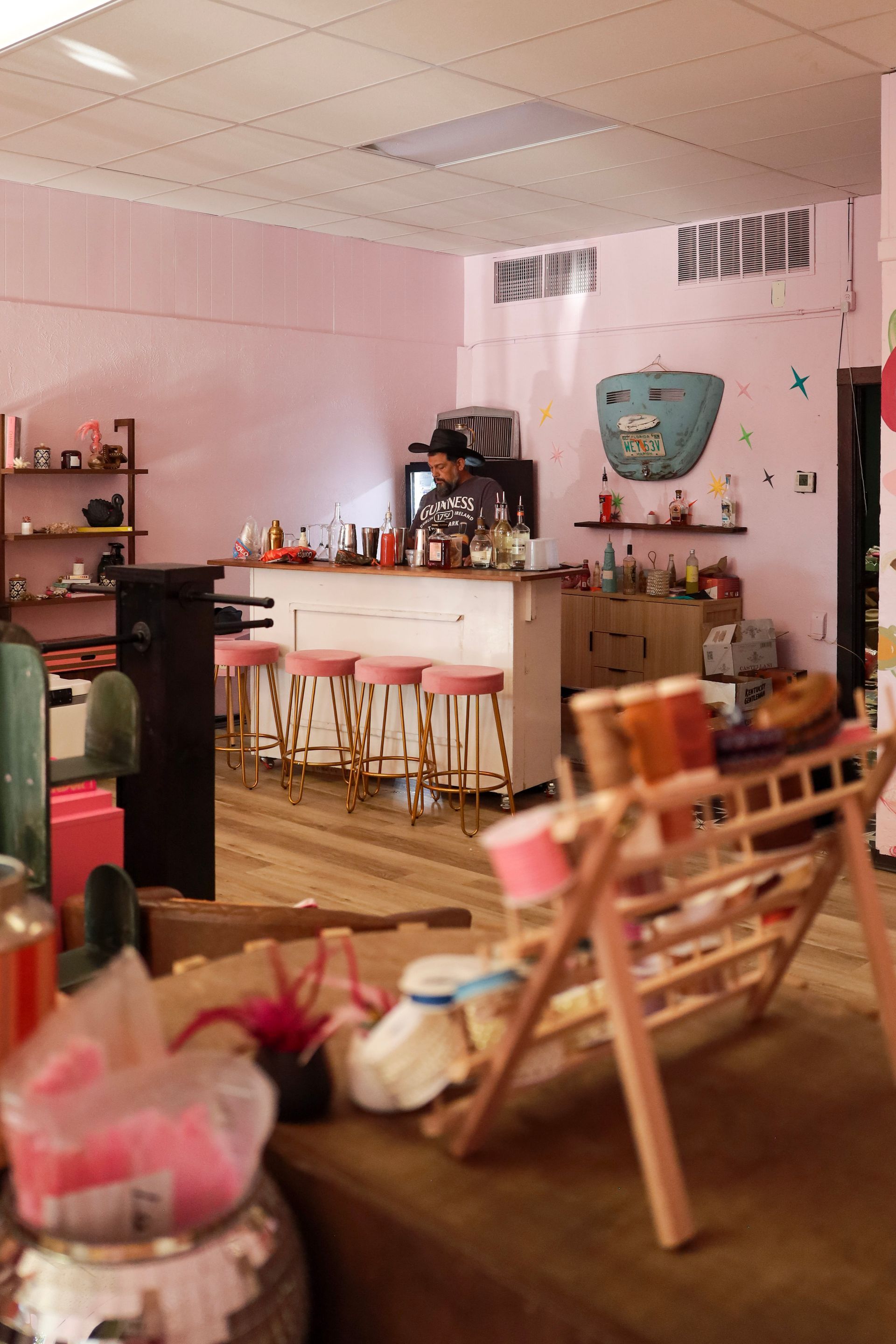 Pink café interior with a bar counter, stools, wooden chairs, and a cozy seating area