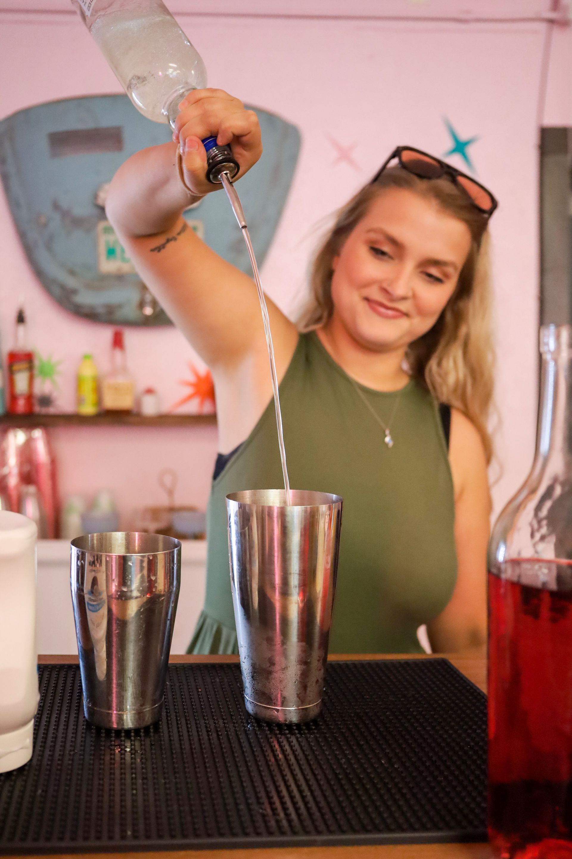 Bartender pouring a clear drink into a metal shaker at a pink cocktail bar