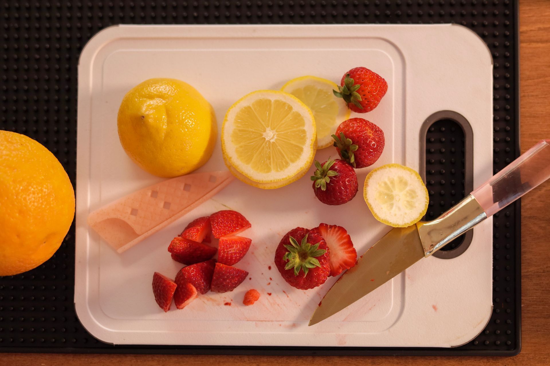 Lemons, strawberries, and a knife on a cutting board, with a hand squeezing lemon juice.