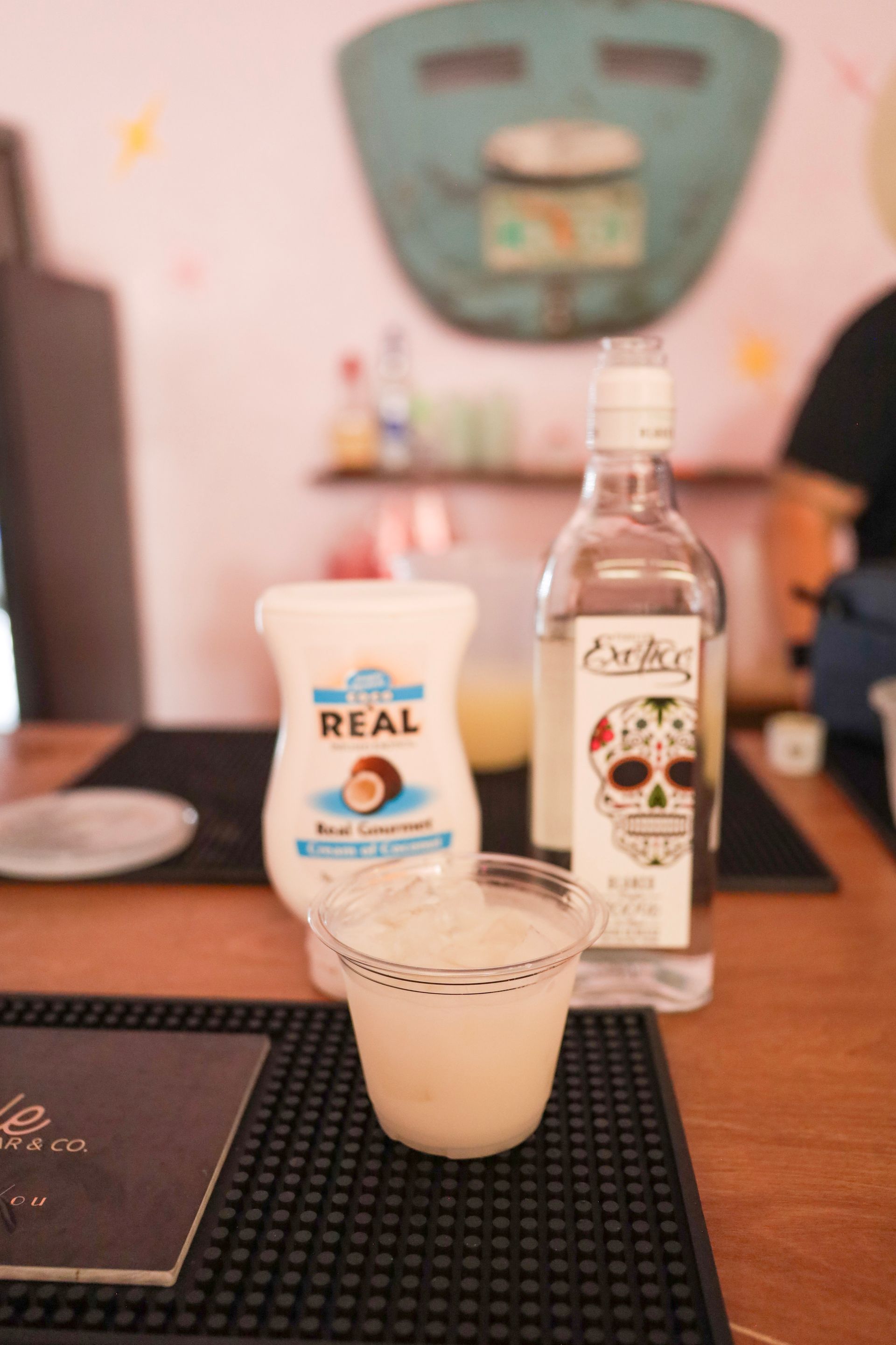 A tabletop with a drink in a cup, a bottle, and a yogurt cup in a softly lit room.