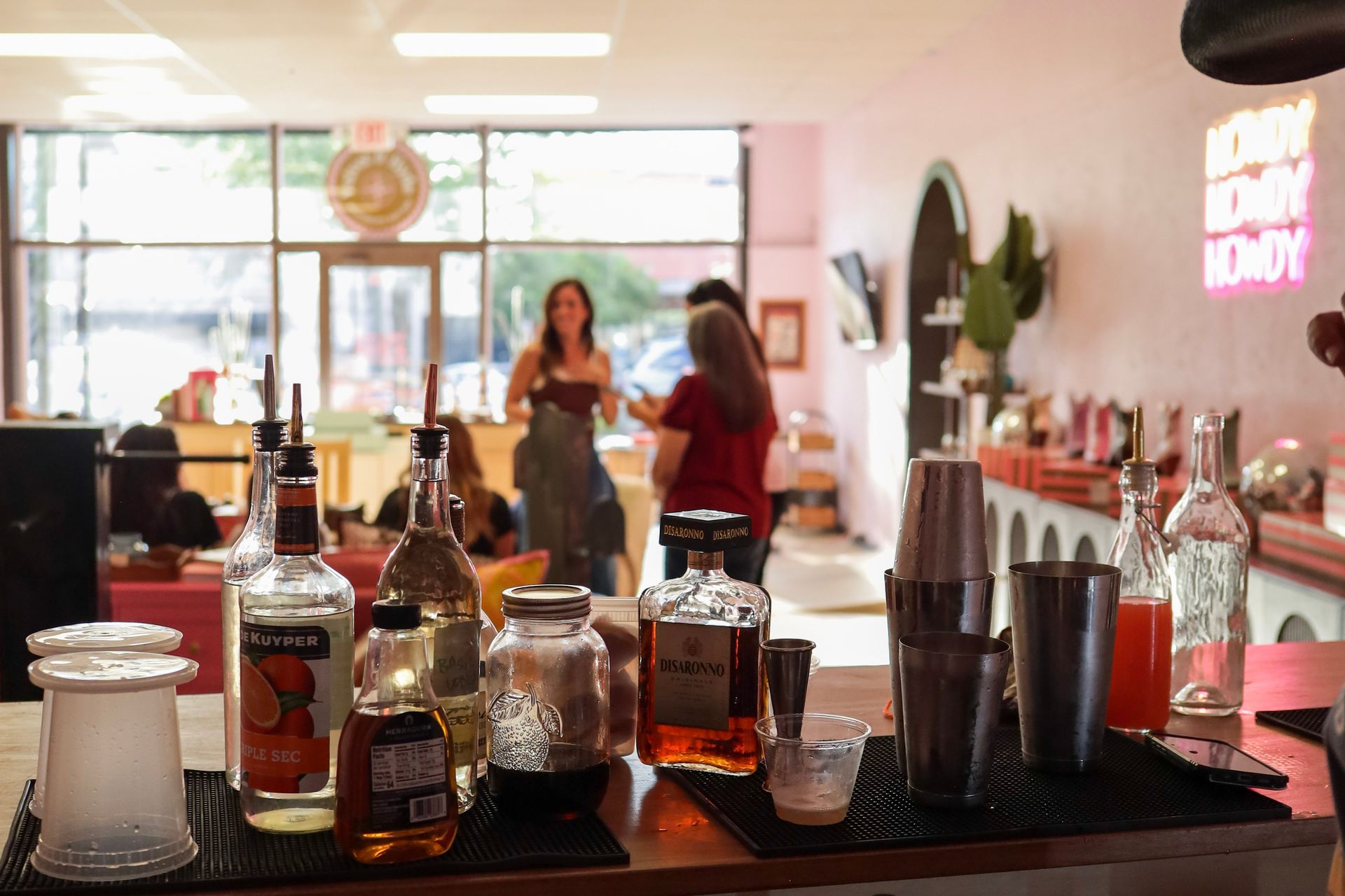 Coffee shop counter with syrups and cups in front of a bright lobby, two people chatting in the background