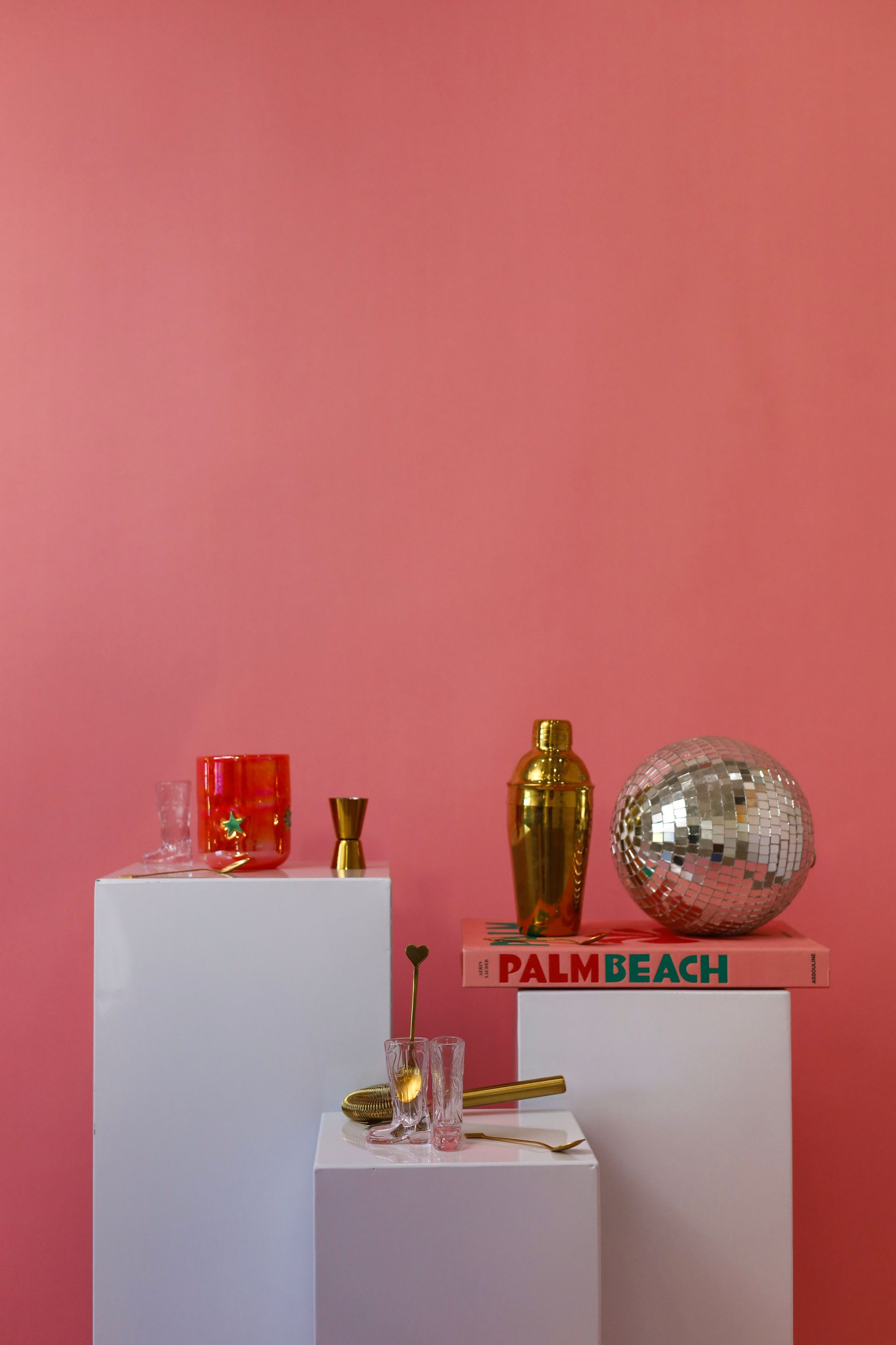 Decorative display of gold and red objects on white pedestals against a pink wall