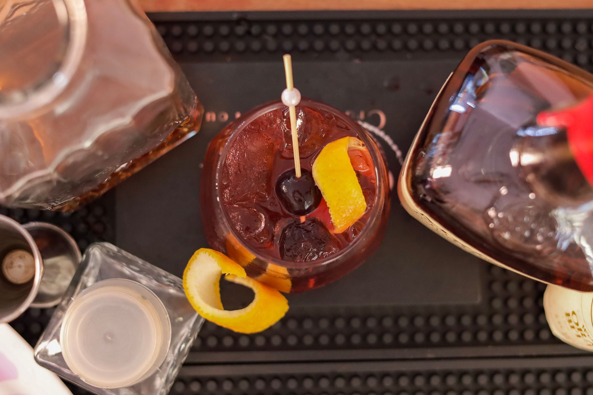 Assorted cocktails on a tray, including a dark red drink with citrus garnish and a cocktail pick.