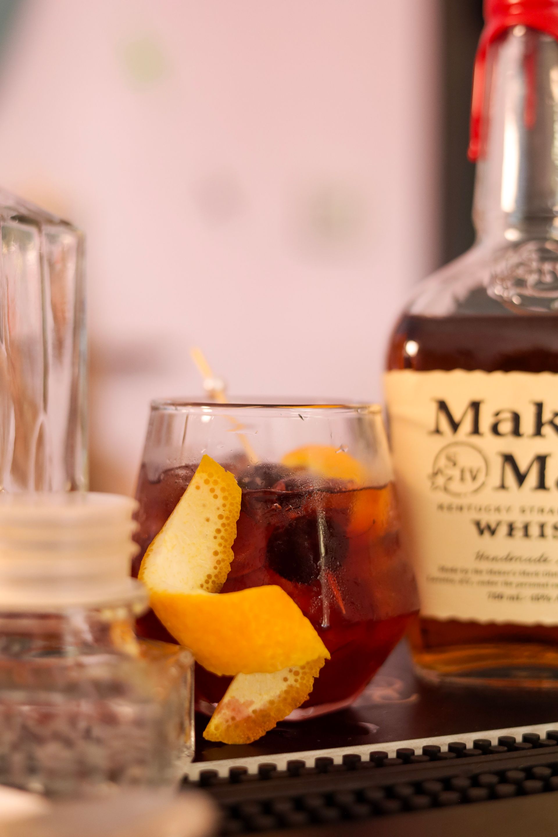 Cocktail with orange peel garnish beside a bottle of whiskey on a bar counter