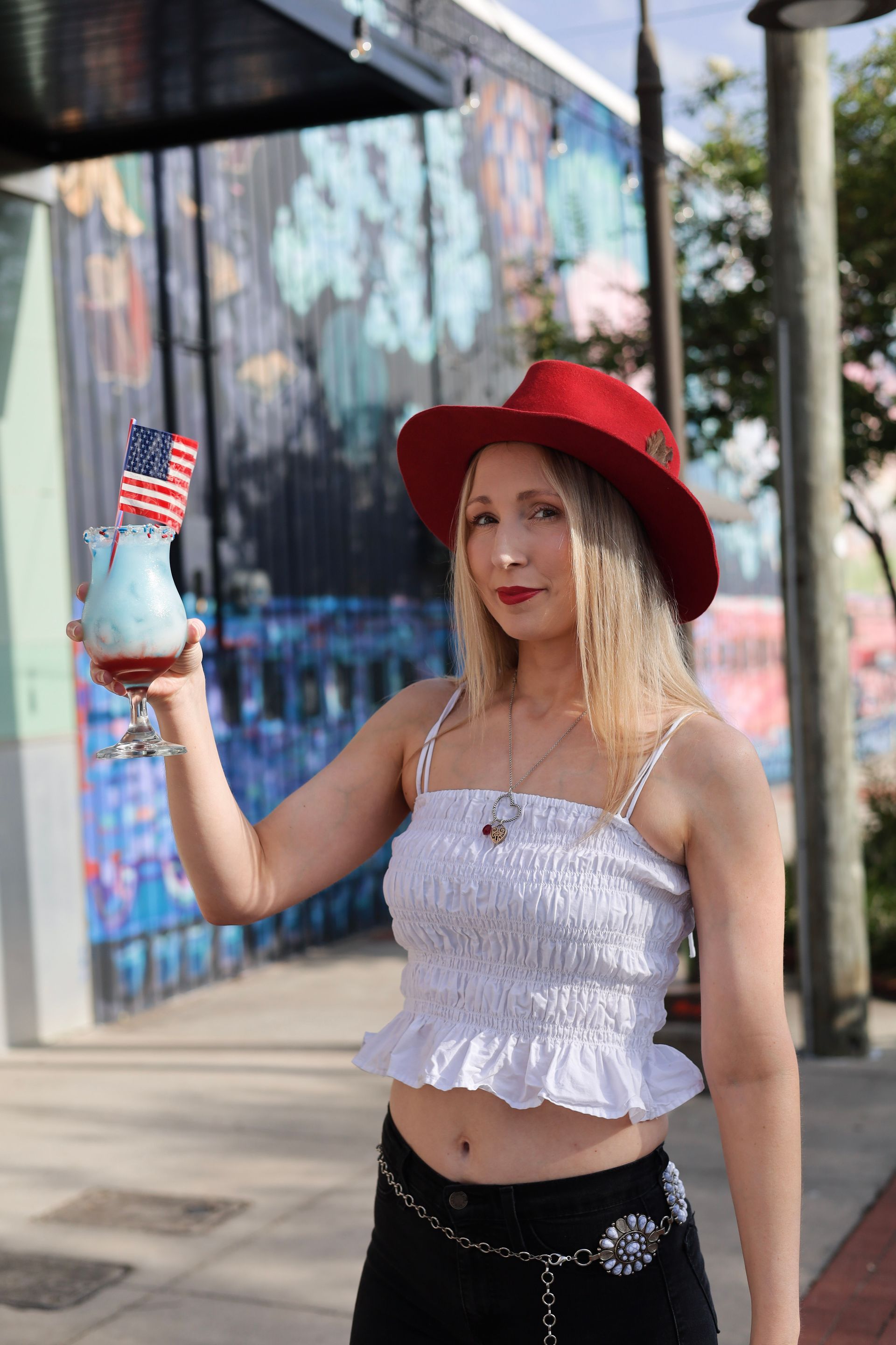 Woman in a red hat holding a blue drink with a small American flag outdoors.