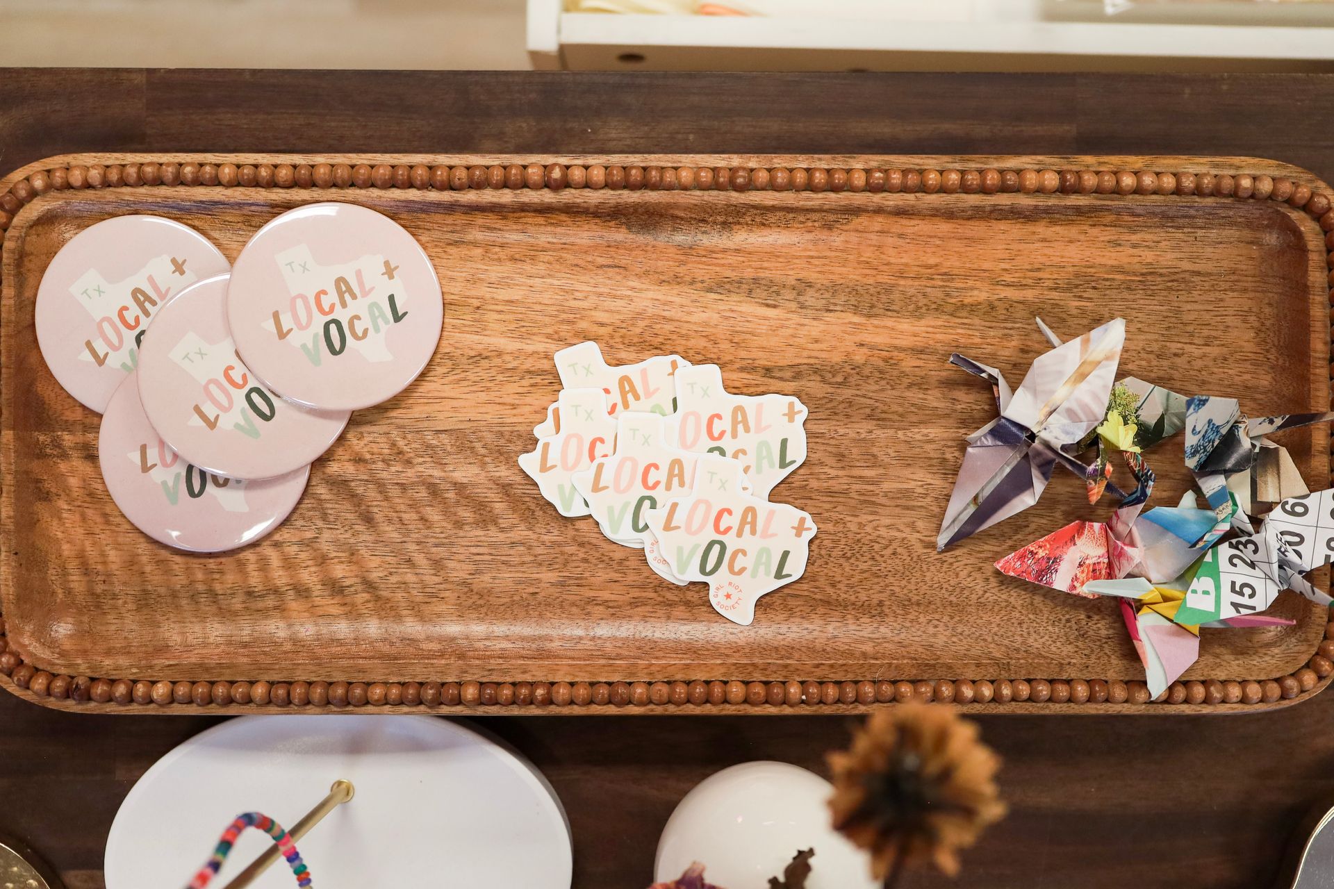 Woven tray with round labels, white scalloped tags, and colorful folded paper pieces on a table.
