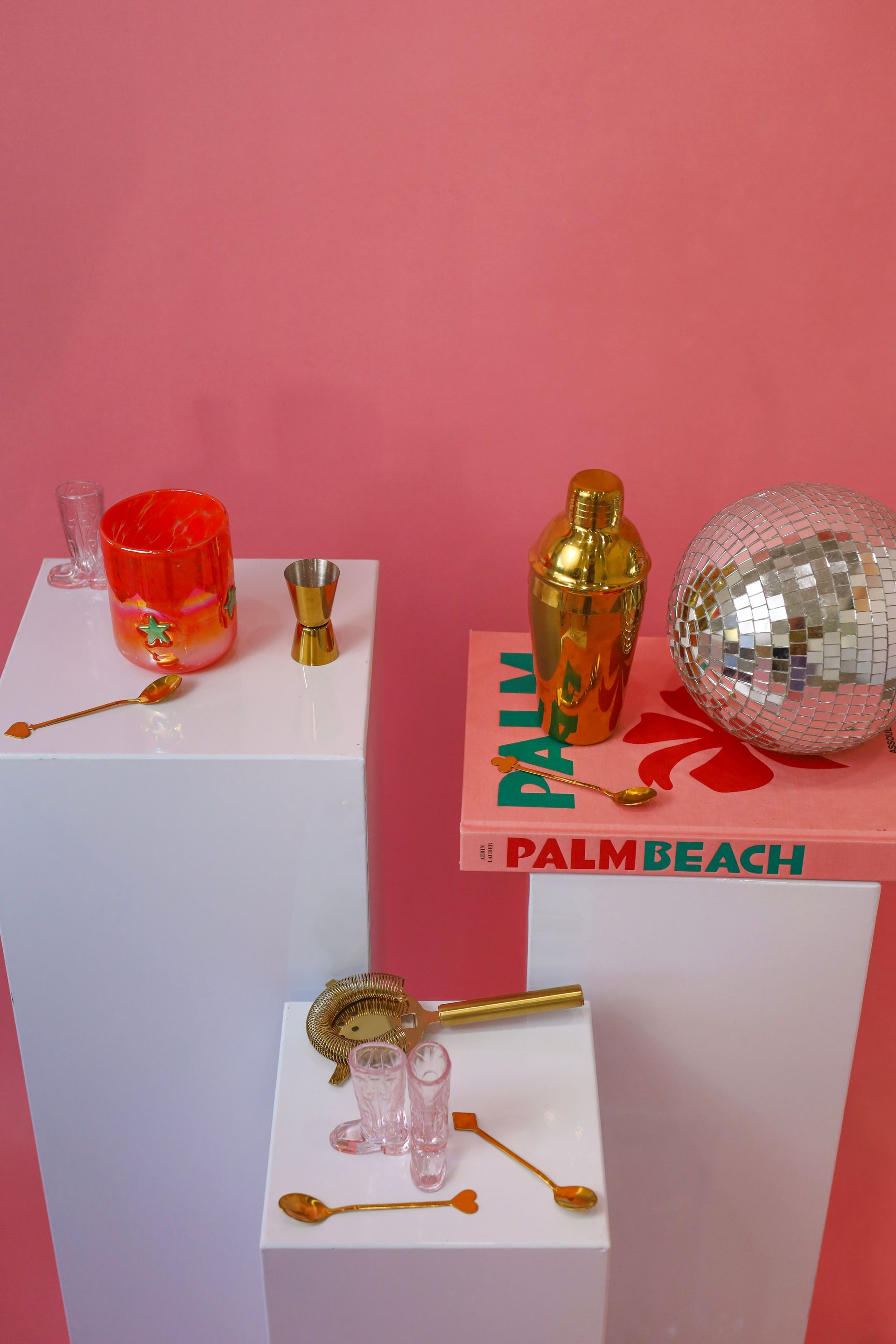 Decorative Christmas display with gold and red ornaments on white pedestals against a pink wall