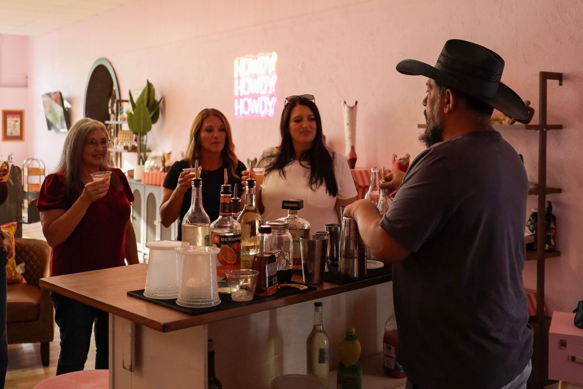 People gathered around a bar cart at a cozy indoor party, chatting with drinks in hand.