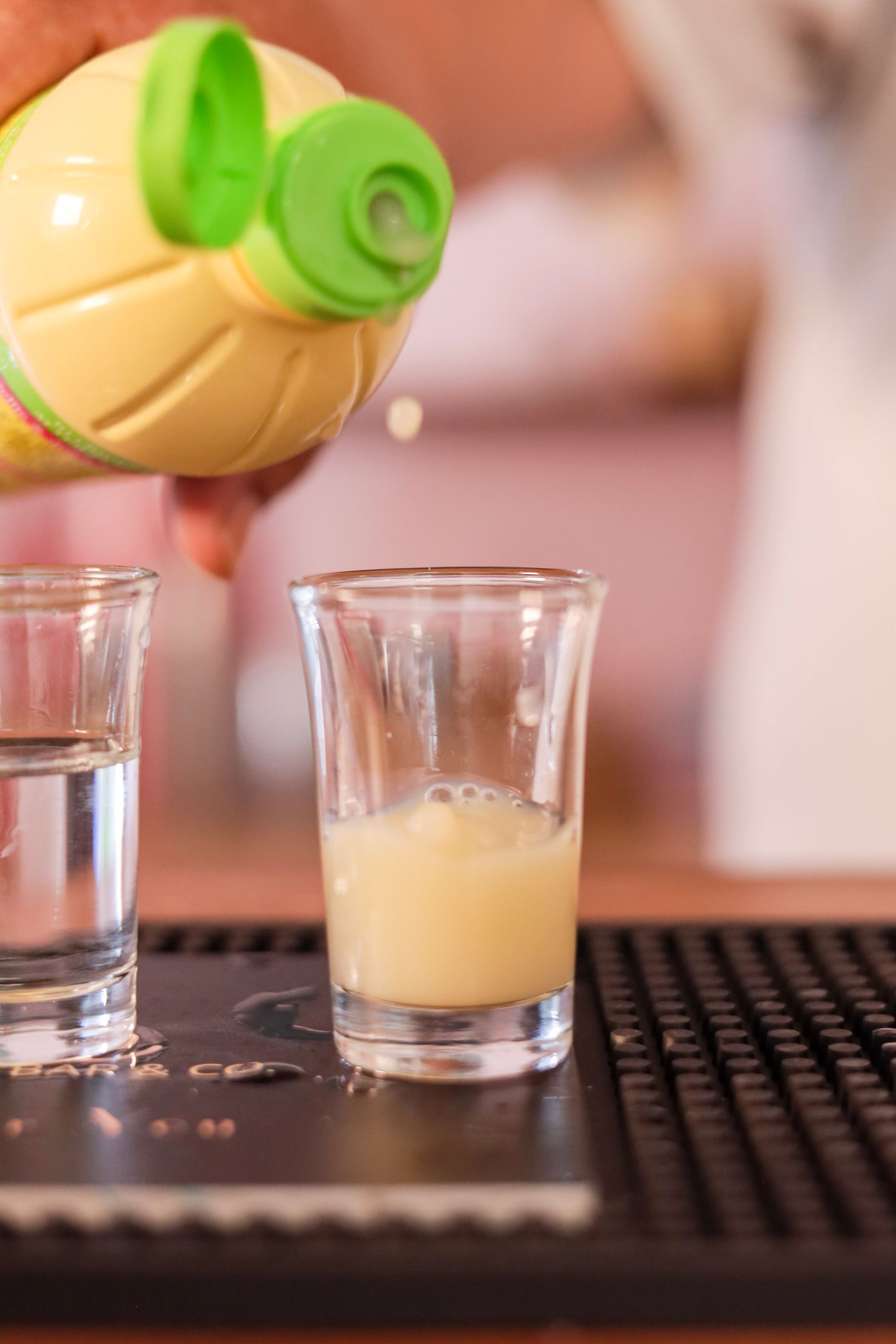 Pouring orange juice into a small glass beside water glasses on a bar counter