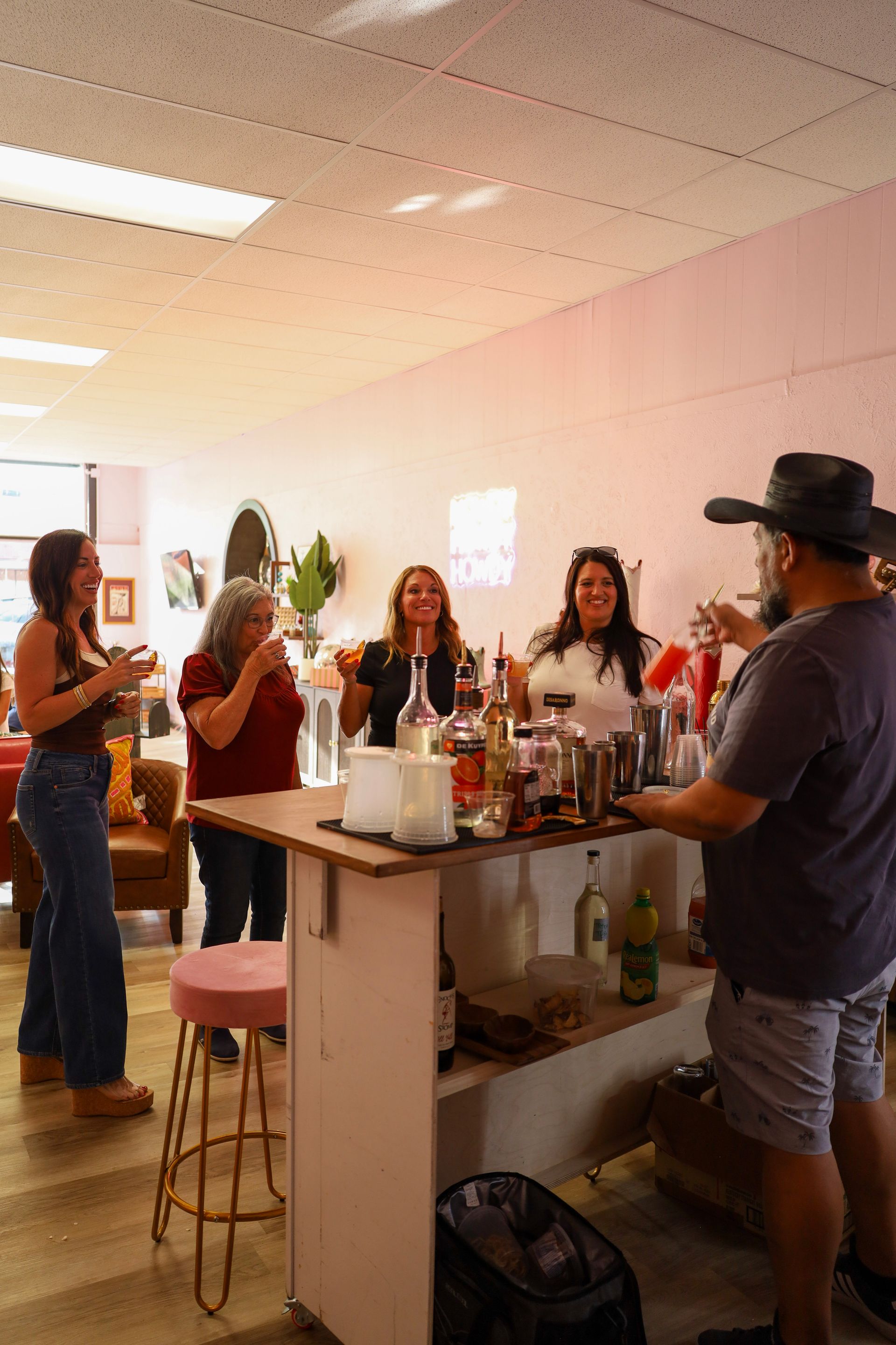 People gathered around a kitchen island at a casual indoor party, with drinks and food on the counter.