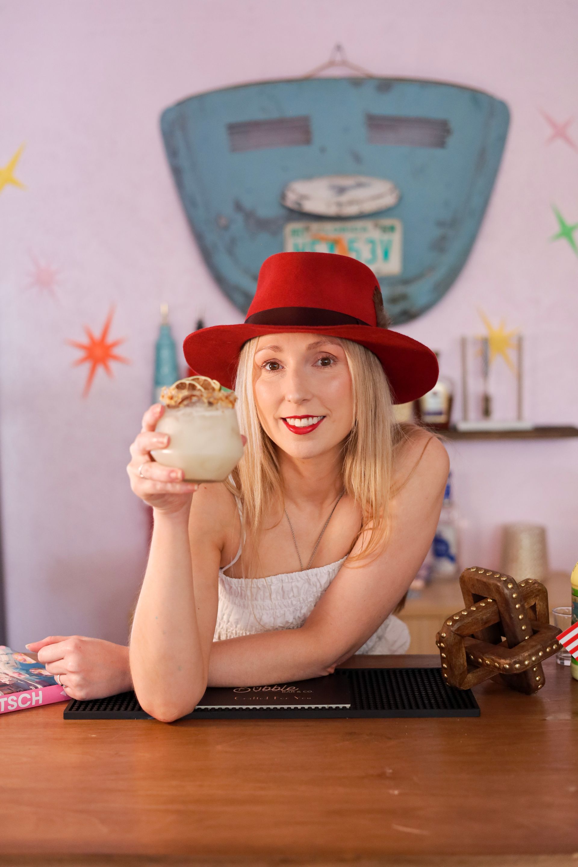 Woman in a red hat holding a jar behind a wooden counter in a colorful room