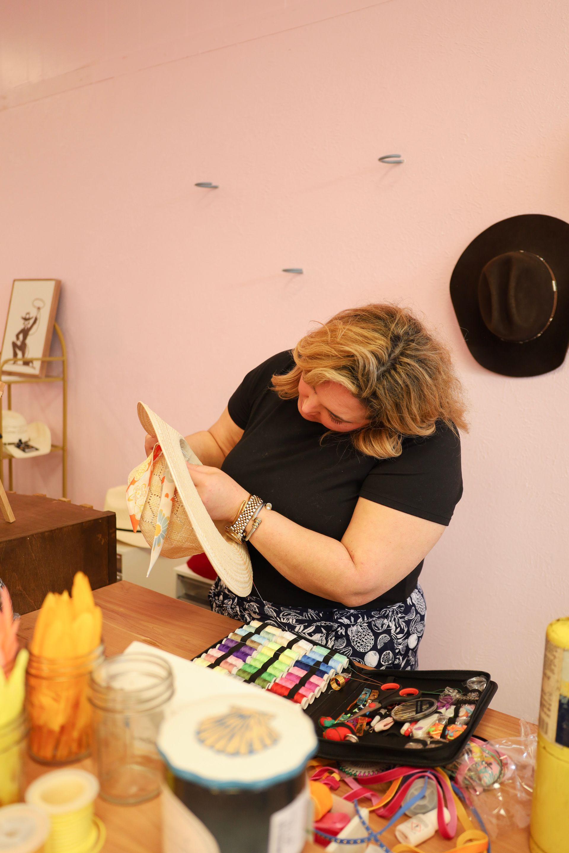 Person painting at a cluttered table, focused on artwork in a pink room.