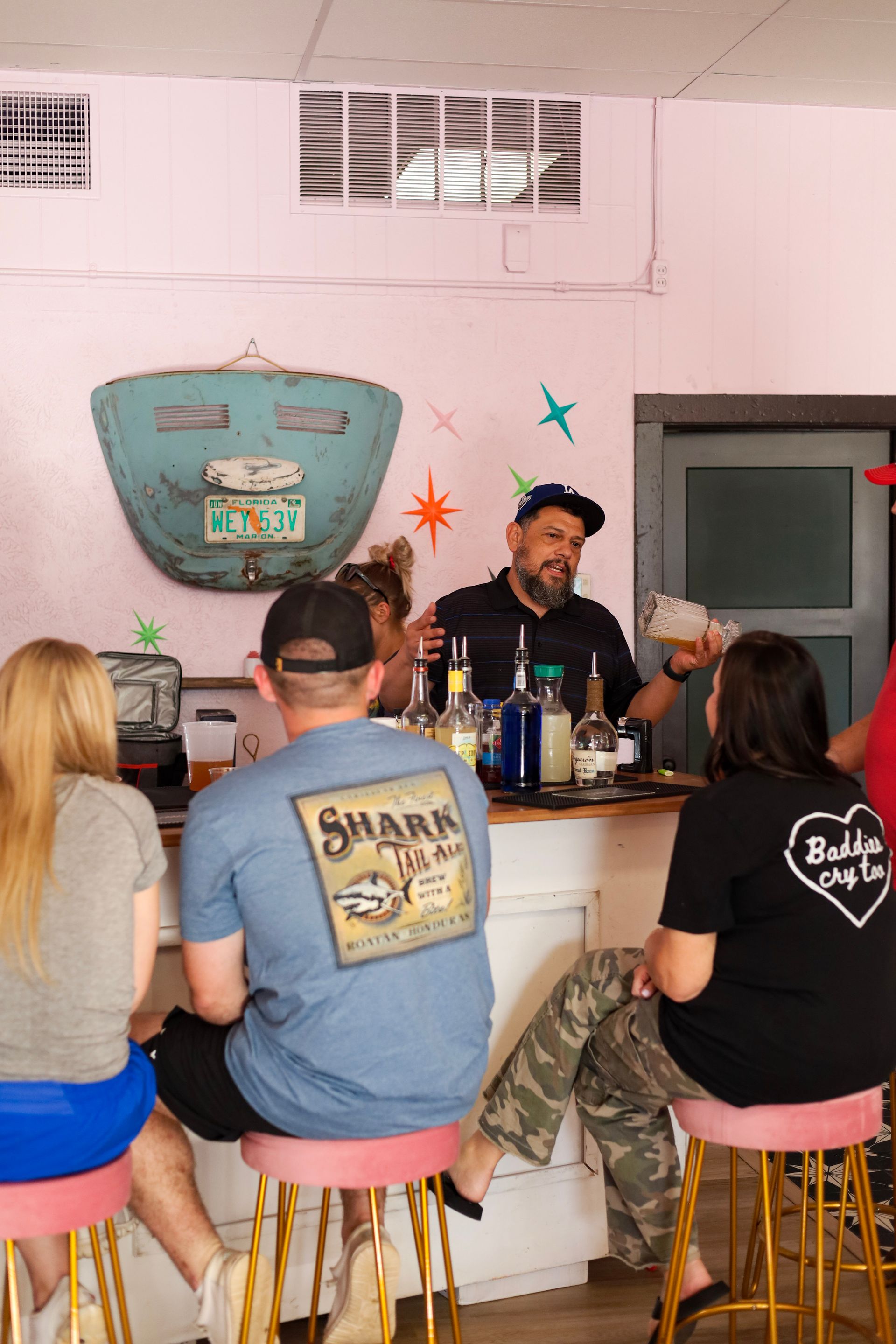 Small café counter with a bartender serving several seated customers in a pink-walled room.