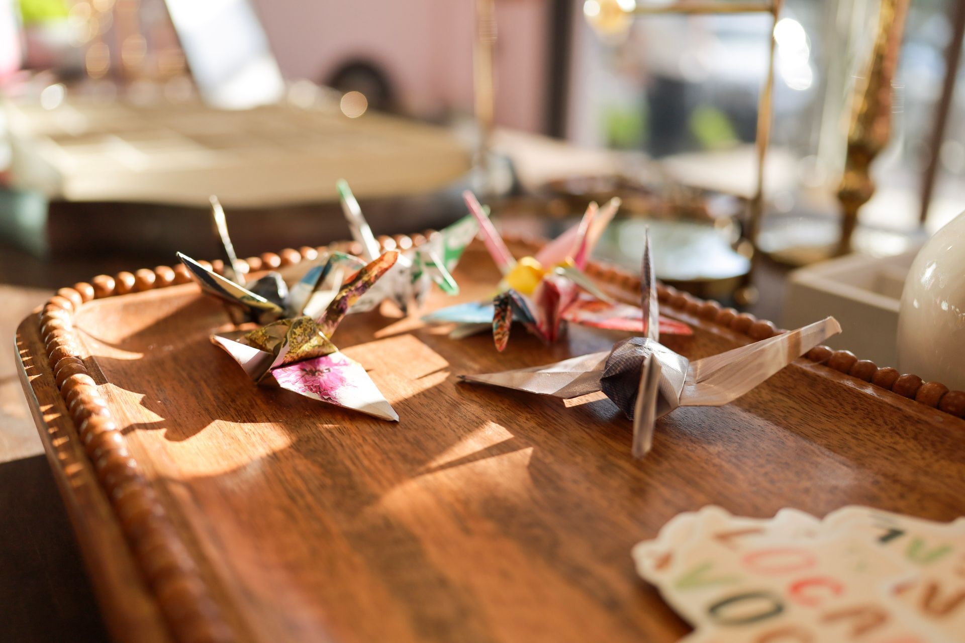 Colorful origami cranes on a wooden tray in a bright indoor setting