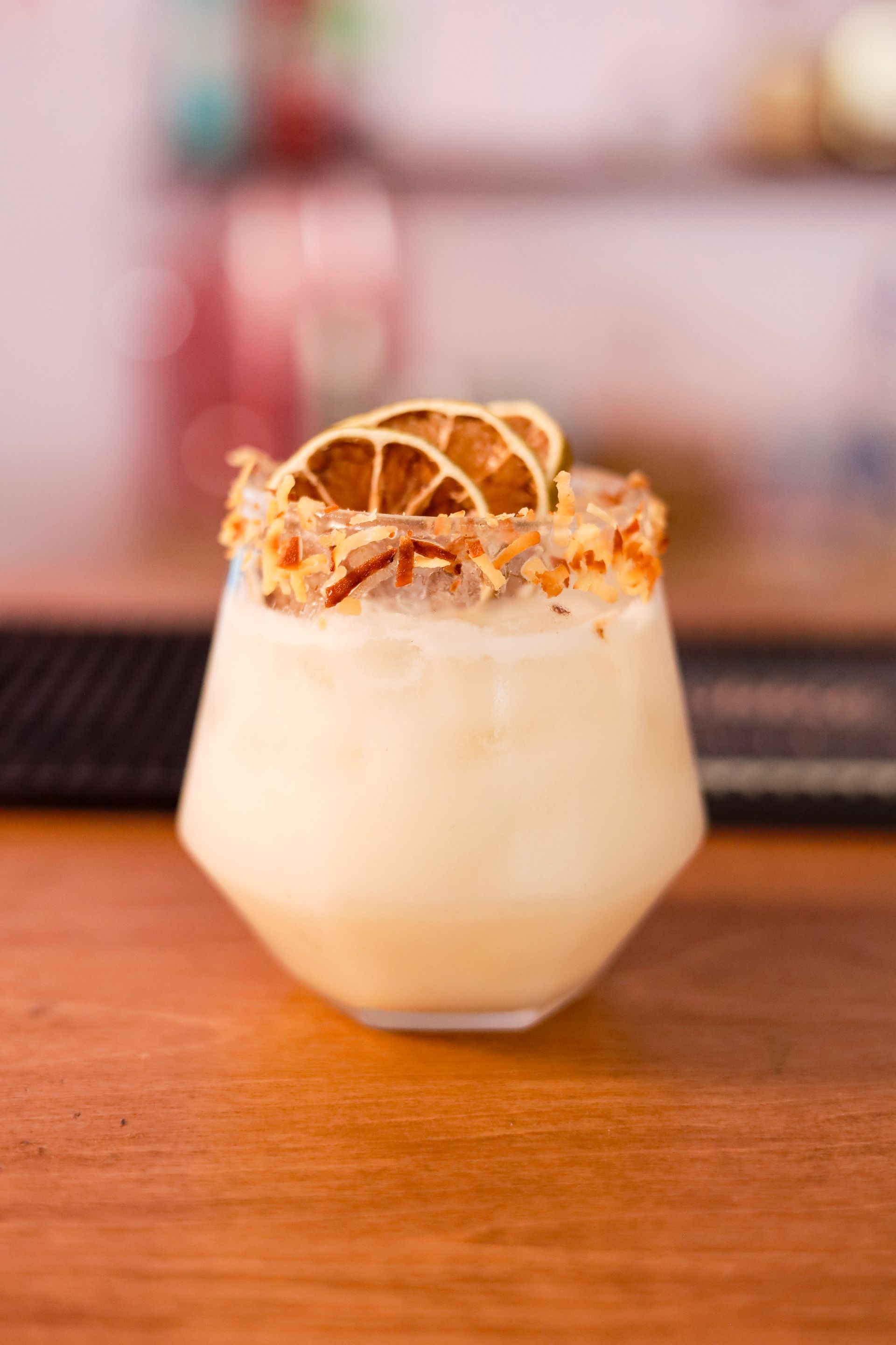 Creamy cocktail in a short glass, topped with dried orange slices, on a wooden bar counter.
