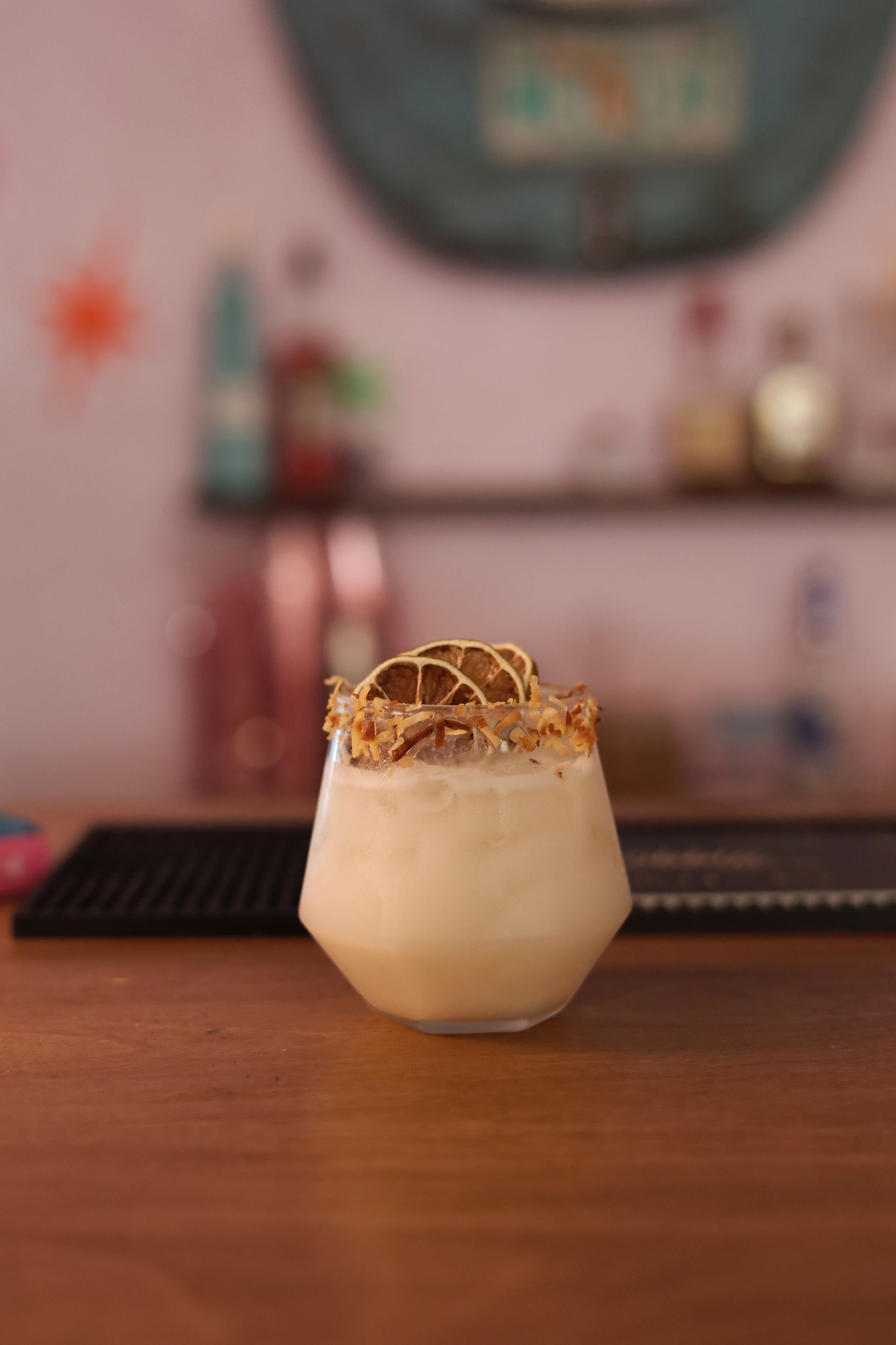 Creamy iced drink topped with herbs in a small glass on a wooden bar counter, with a blurred café background