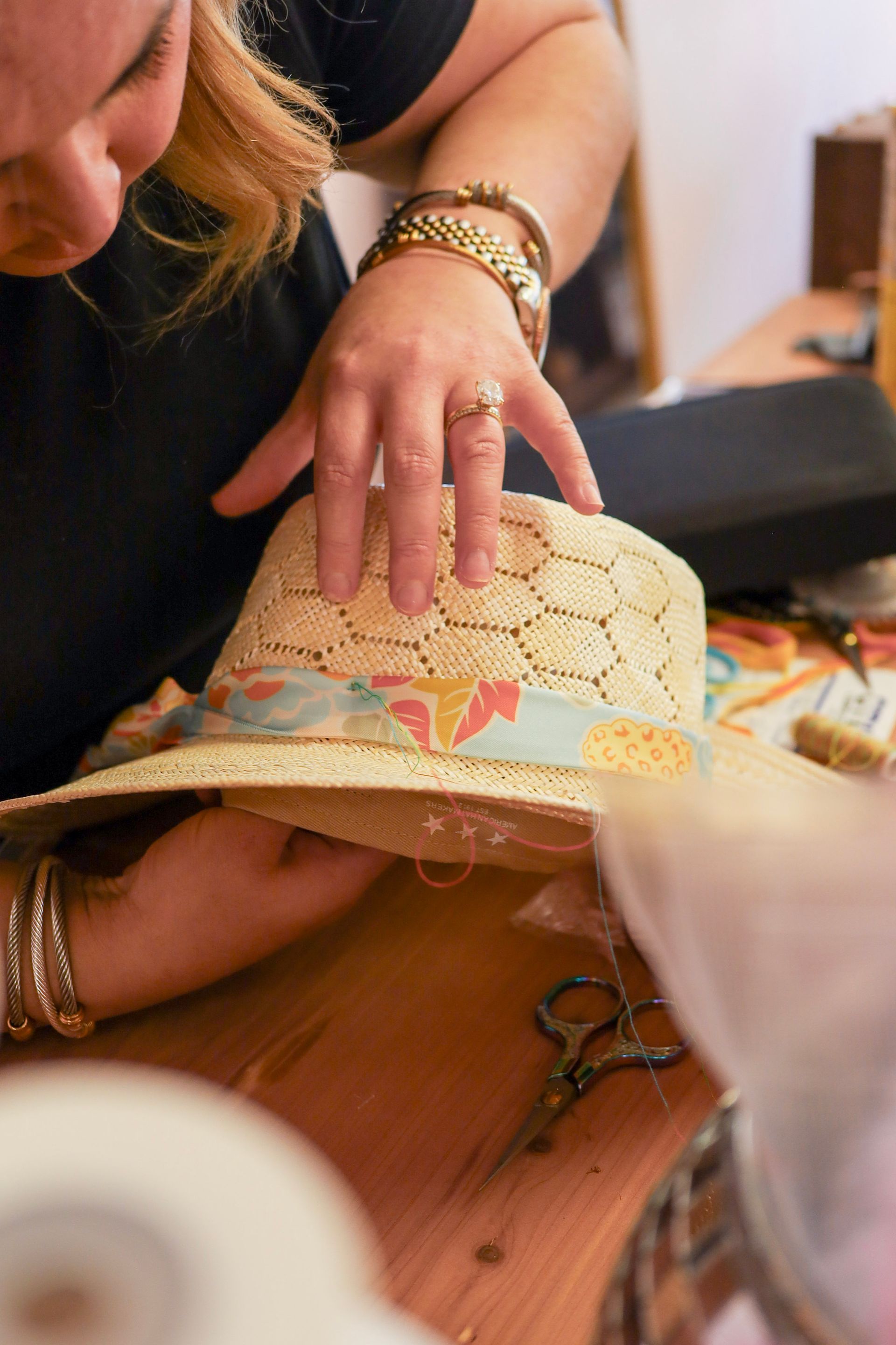Hand decorating a straw hat with a floral ribbon on a wooden table