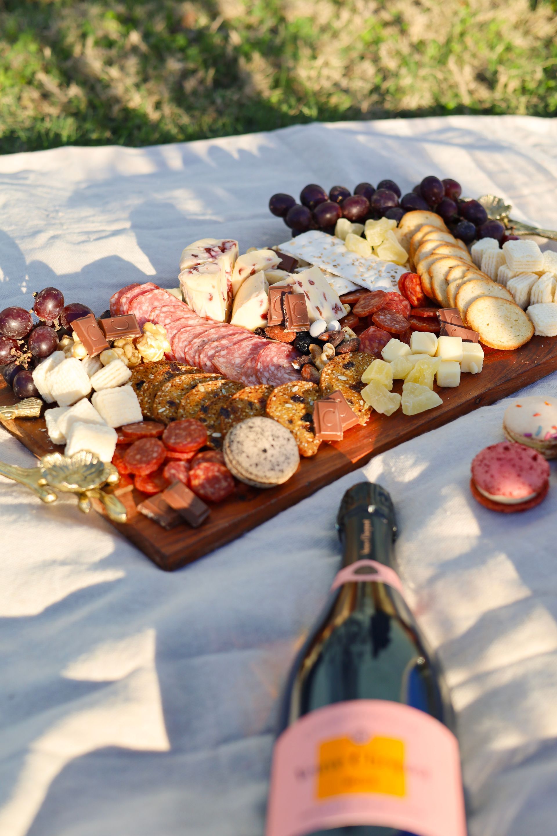 Charcuterie board with cheese, meats, fruit, crackers, and a wine bottle on a picnic blanket