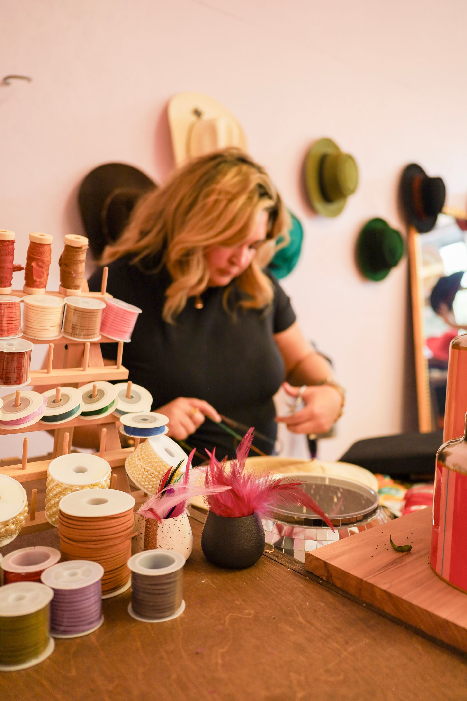 Woman arranging craft supplies at a booth with colorful spools and hats on the wall