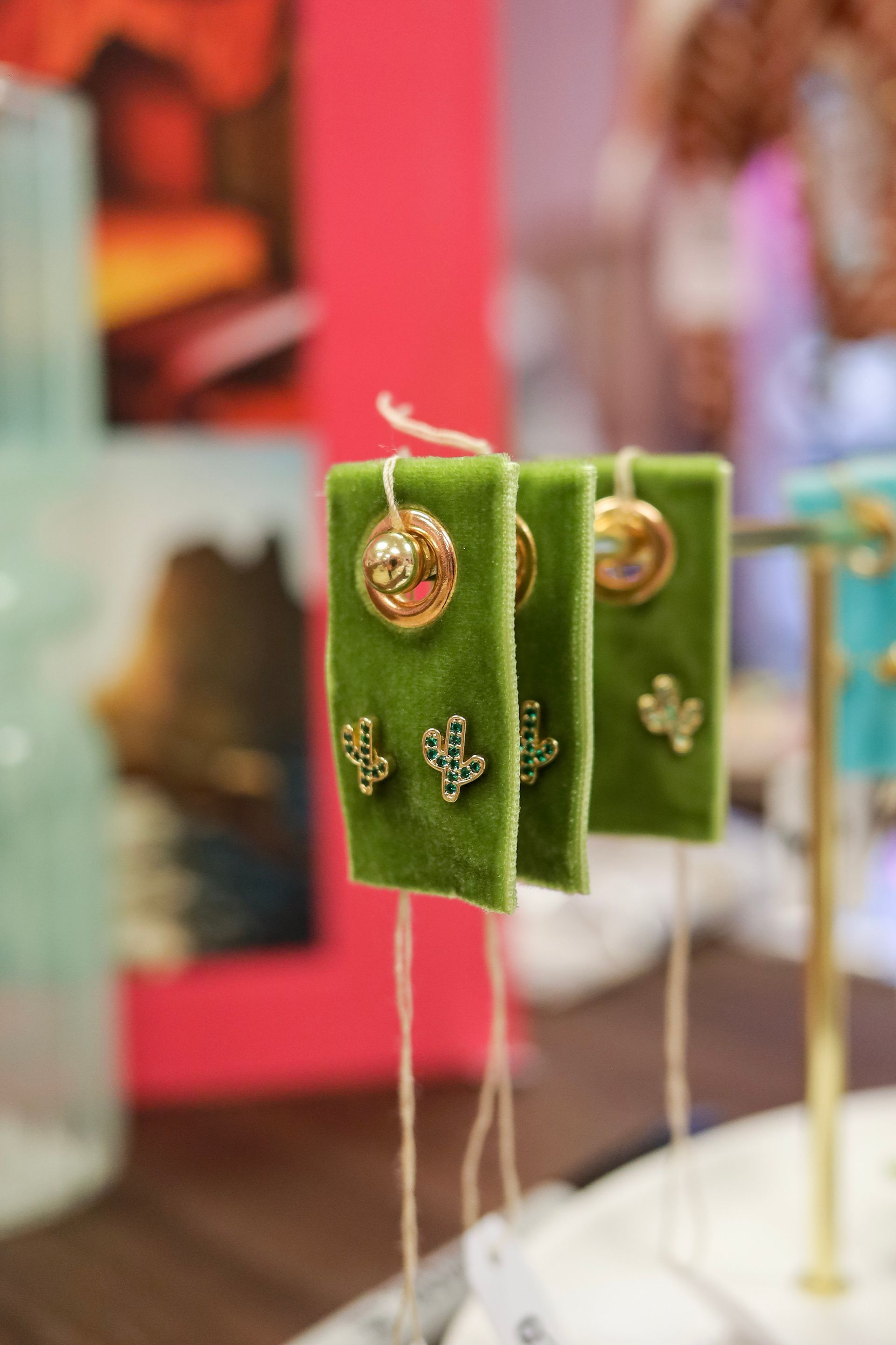 Green velvet earrings on display stands at a jewelry stall, with gold accents and dangling beaded strings.