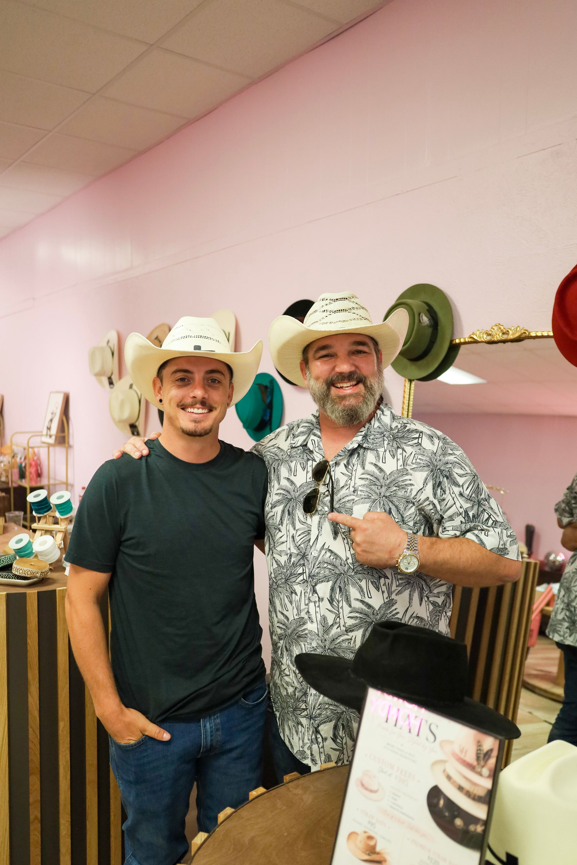 Two men in cowboy hats smiling at a party with pink walls and festive decorations